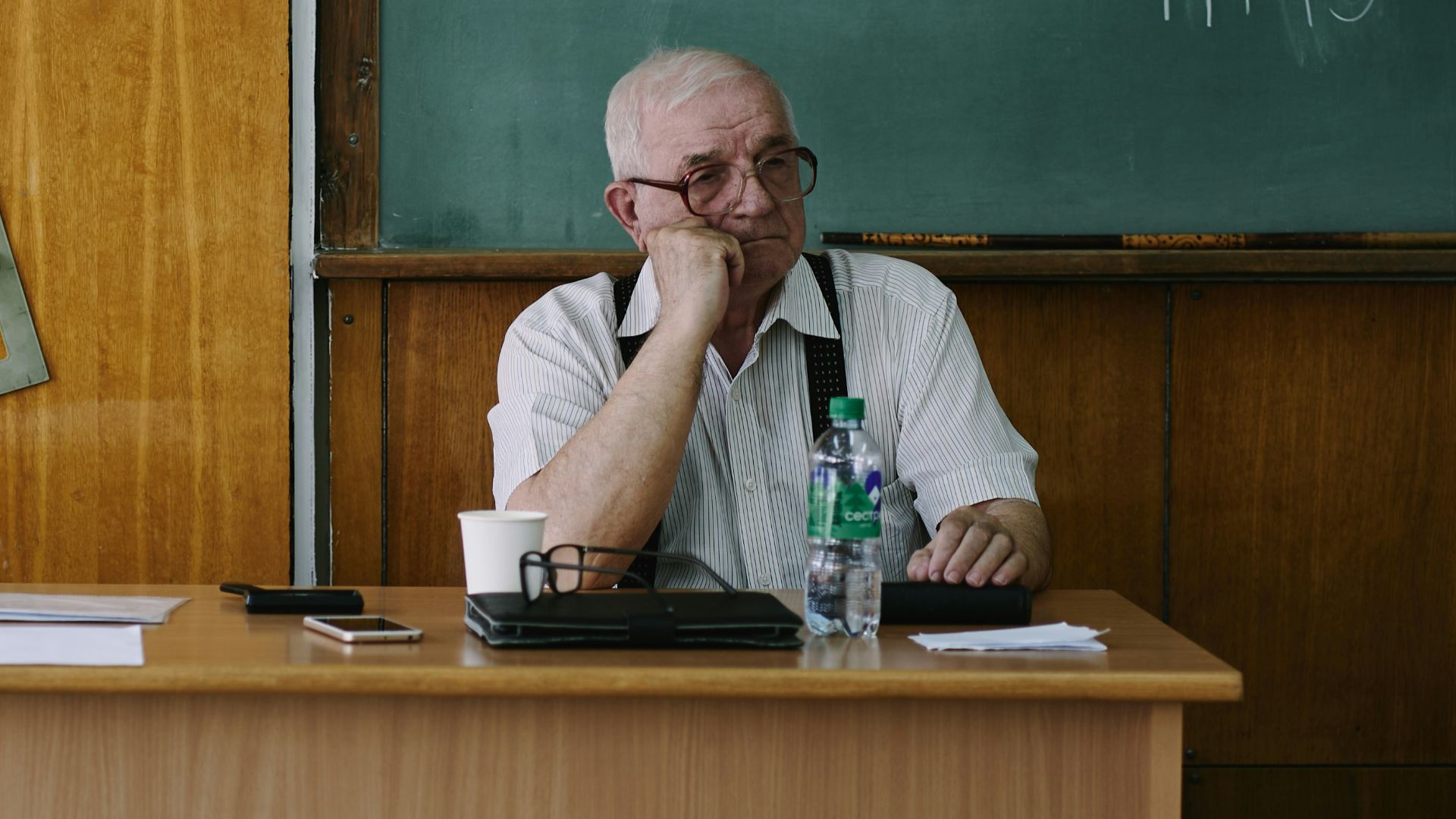 A teacher sits at his desk in a classroom.