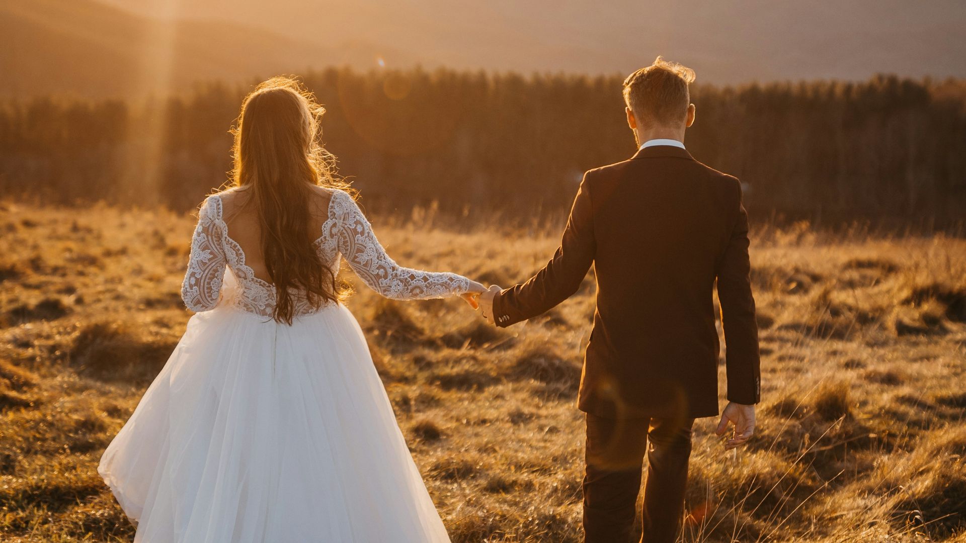 man and woman in wedding dress walking on brown grass field during daytime