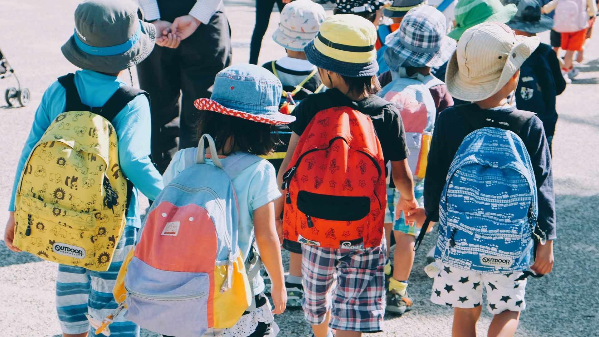 group of people wearing white and orange backpacks walking on gray concrete pavement during daytime