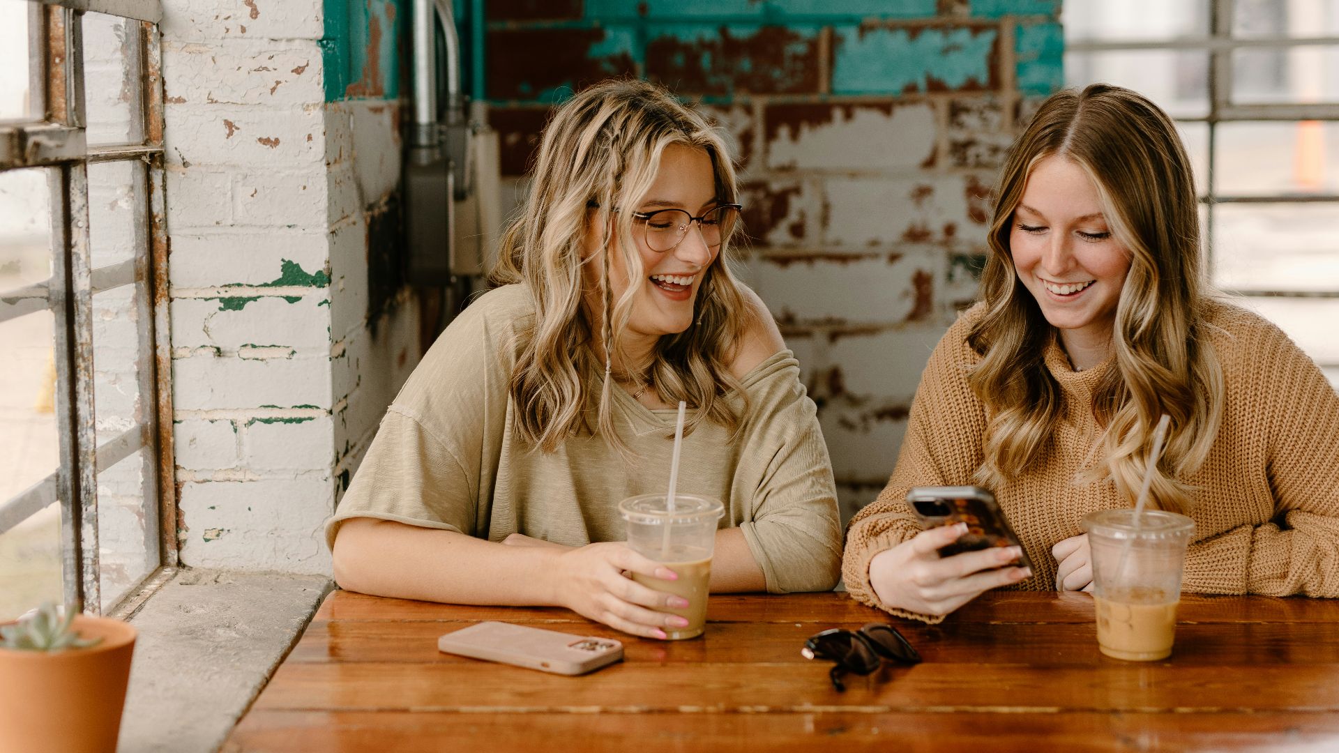 two women sitting at a table looking at a cell phone