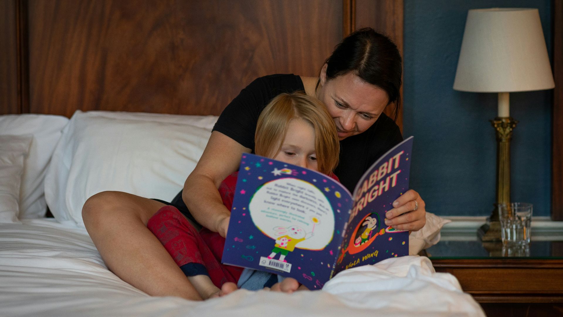 girl in red shirt lying on bed reading book