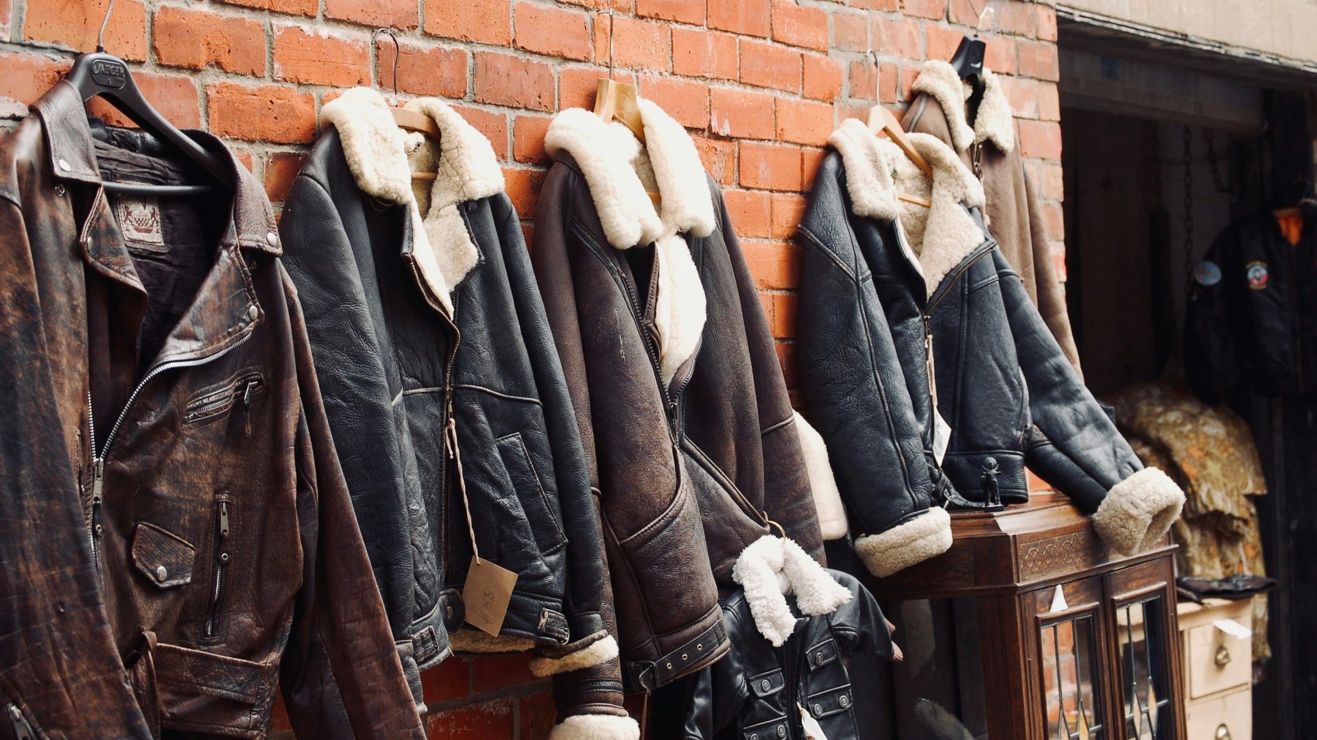 four assorted leather jackets hanging on brown brick wall