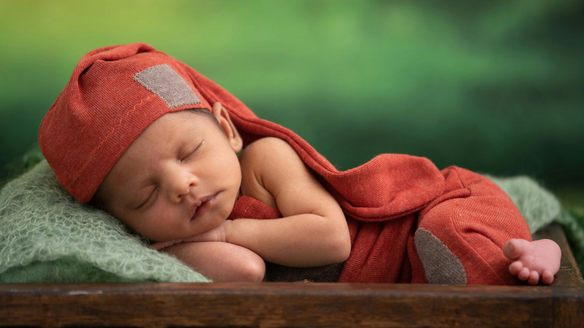 baby in red blanket lying on green textile