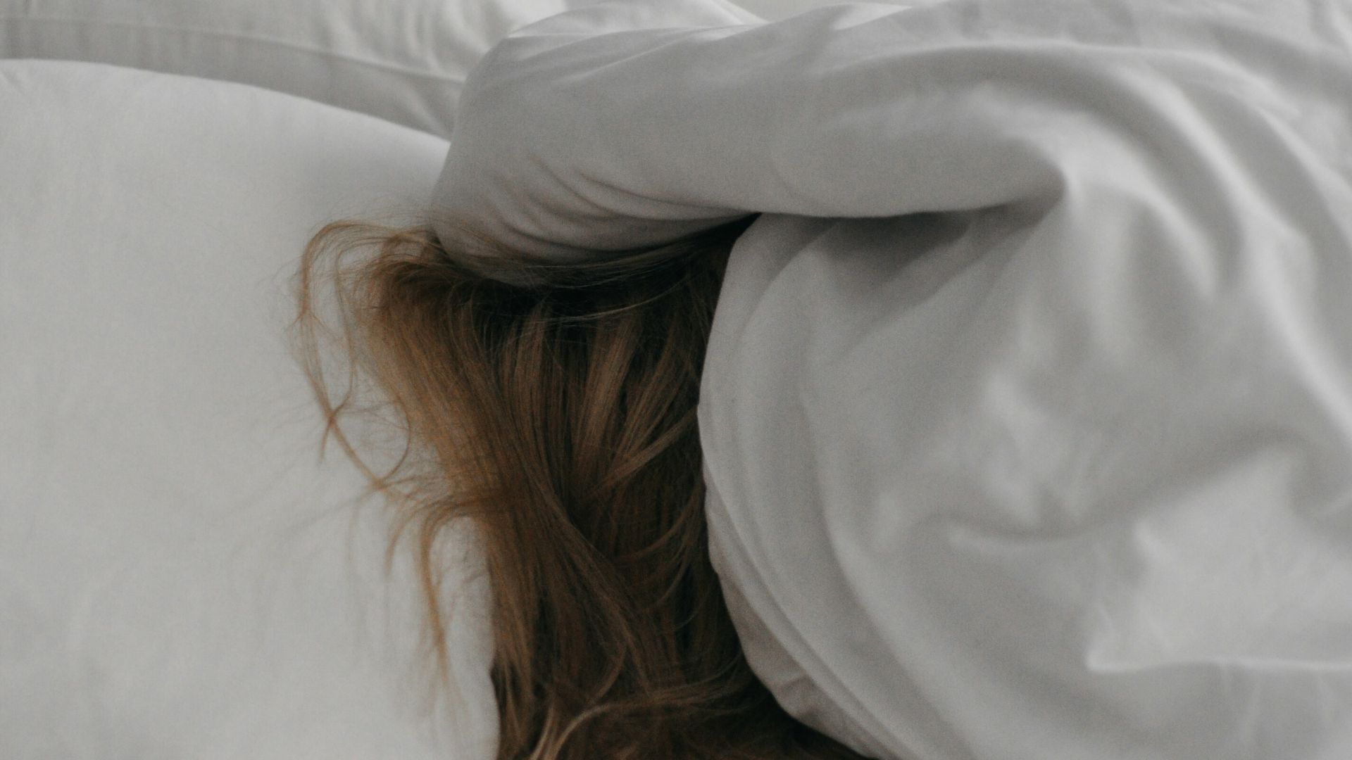 a woman is hiding under a blanket on a bed