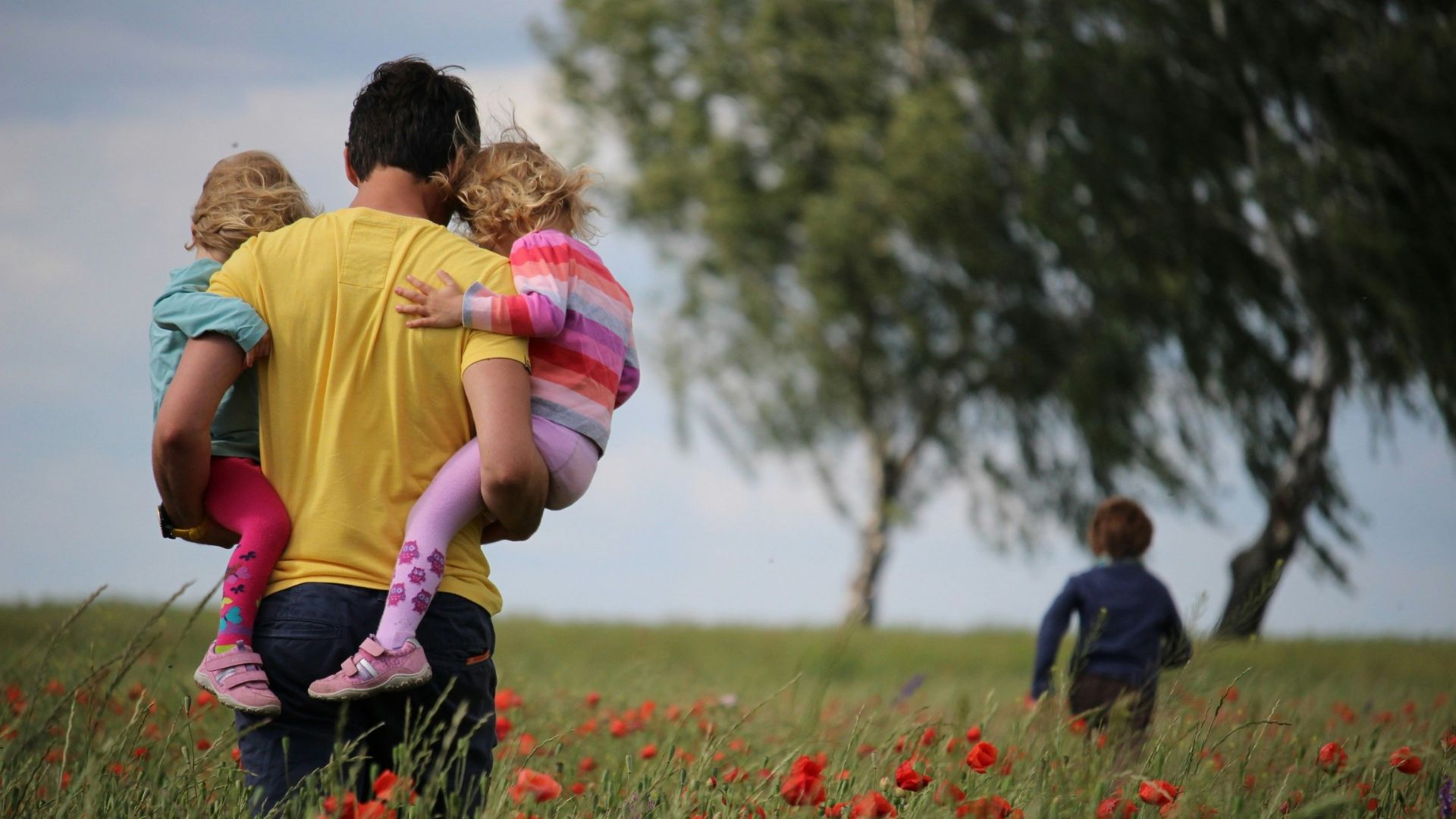 man carrying to girls on field of red petaled flower