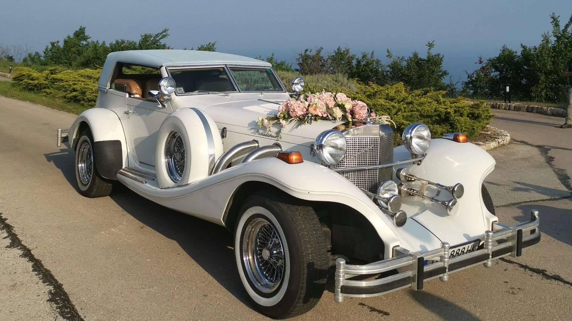 vintage white car with flower decorations in front beside green field