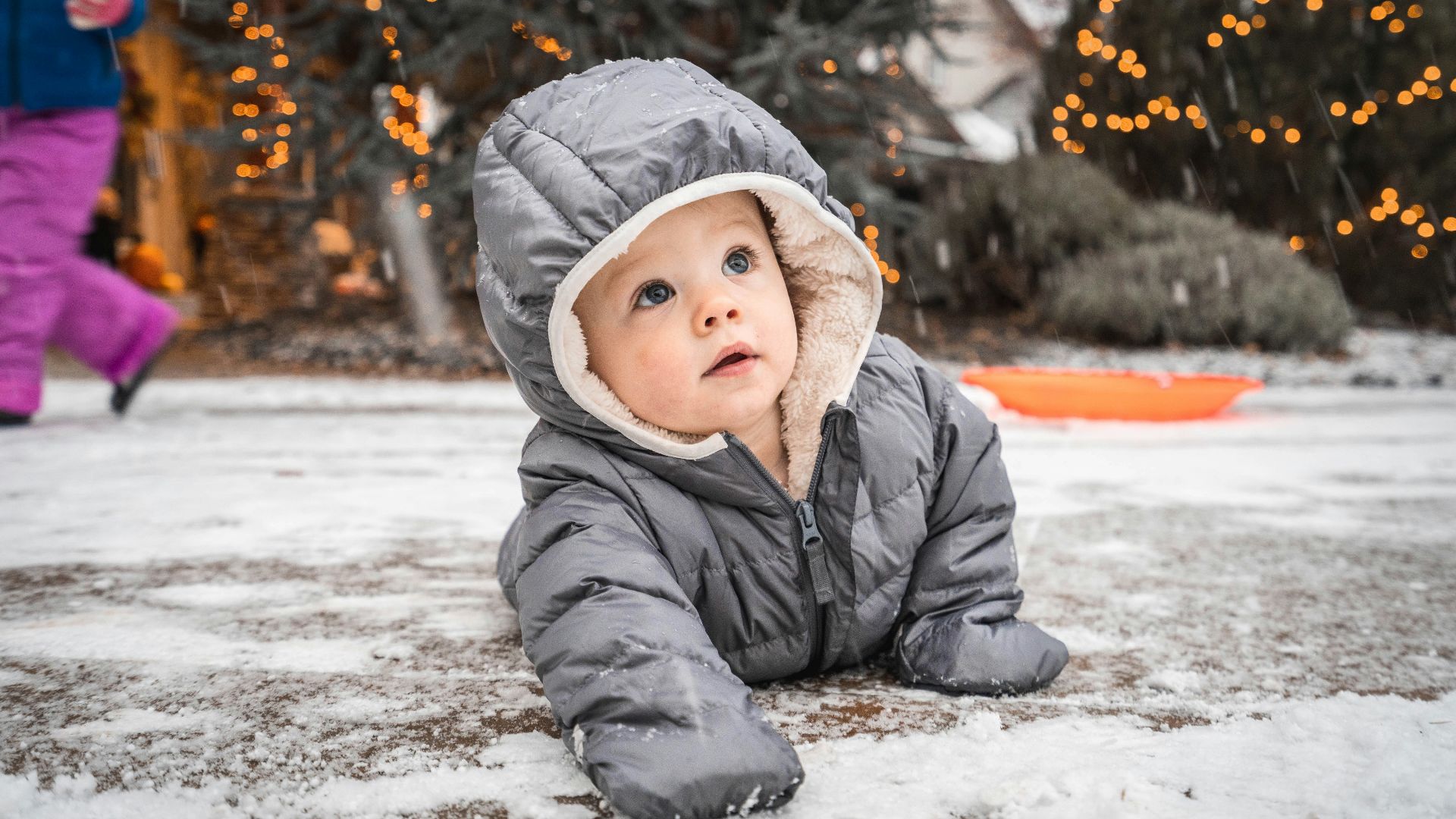 child in gray winter jacket lying on snow covered ground