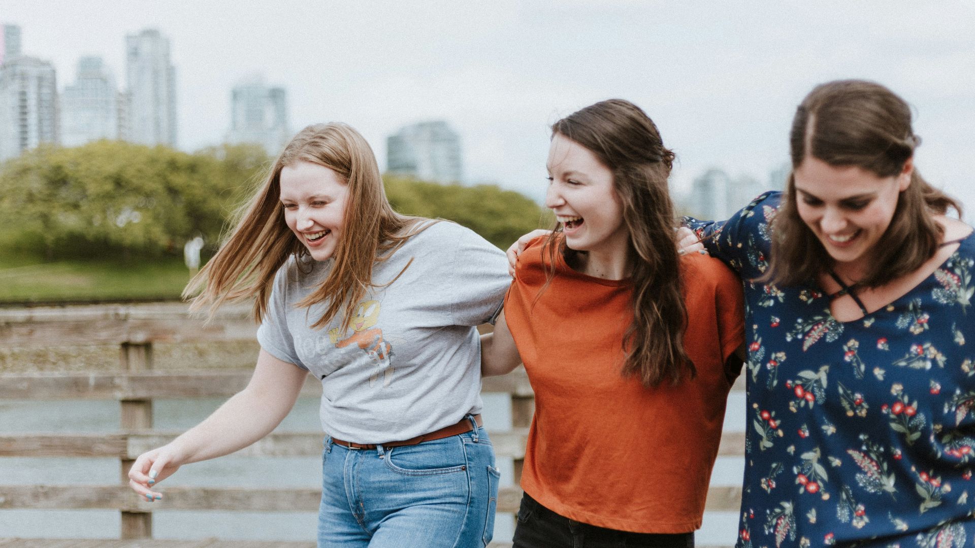 three women walking on brown wooden dock near high rise building during daytime
