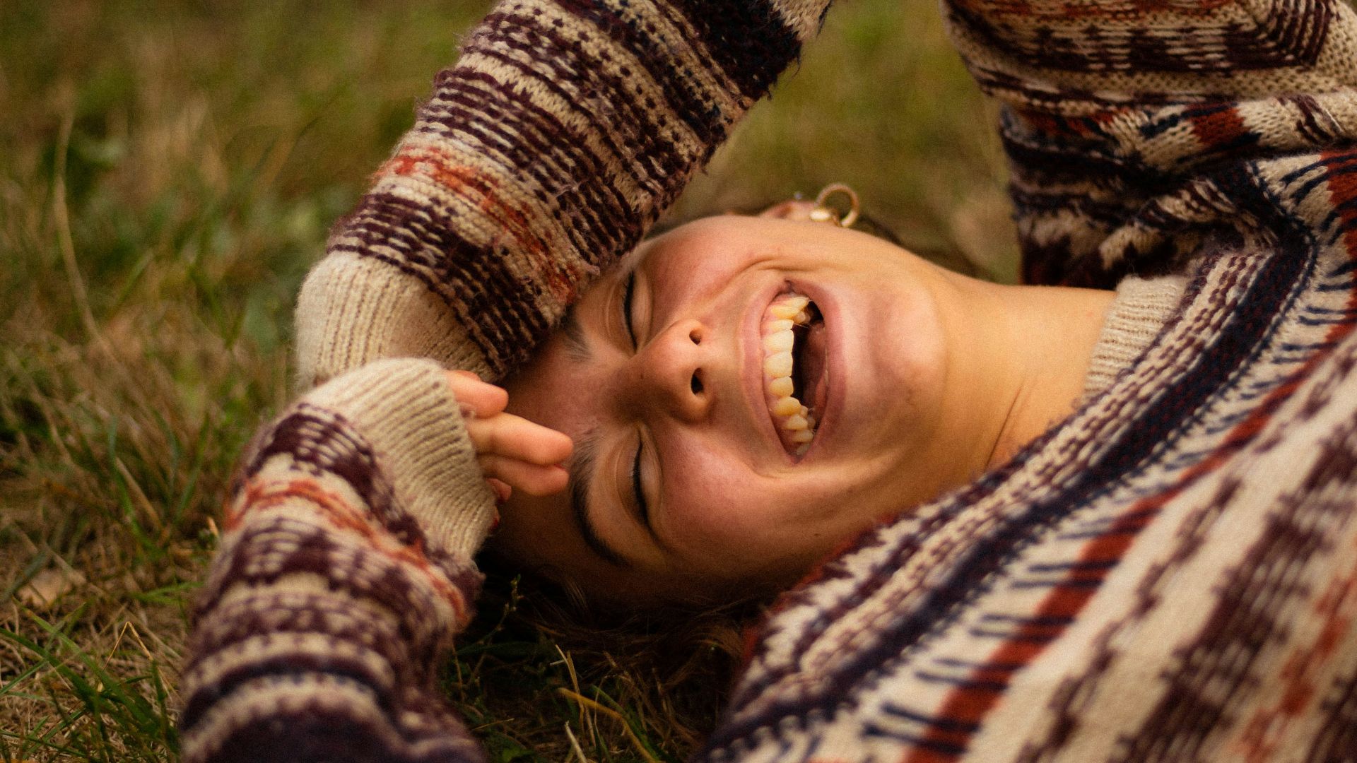woman in brown and white sweater lying on green grass field during daytime
