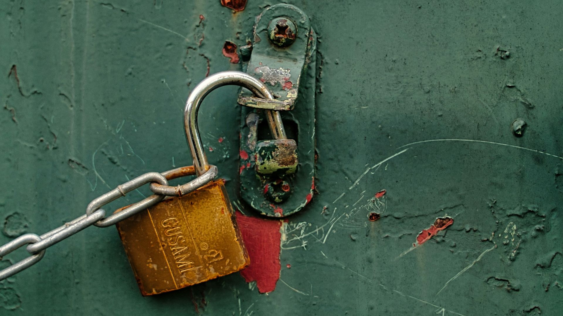 A padlock and chain secure a green door.