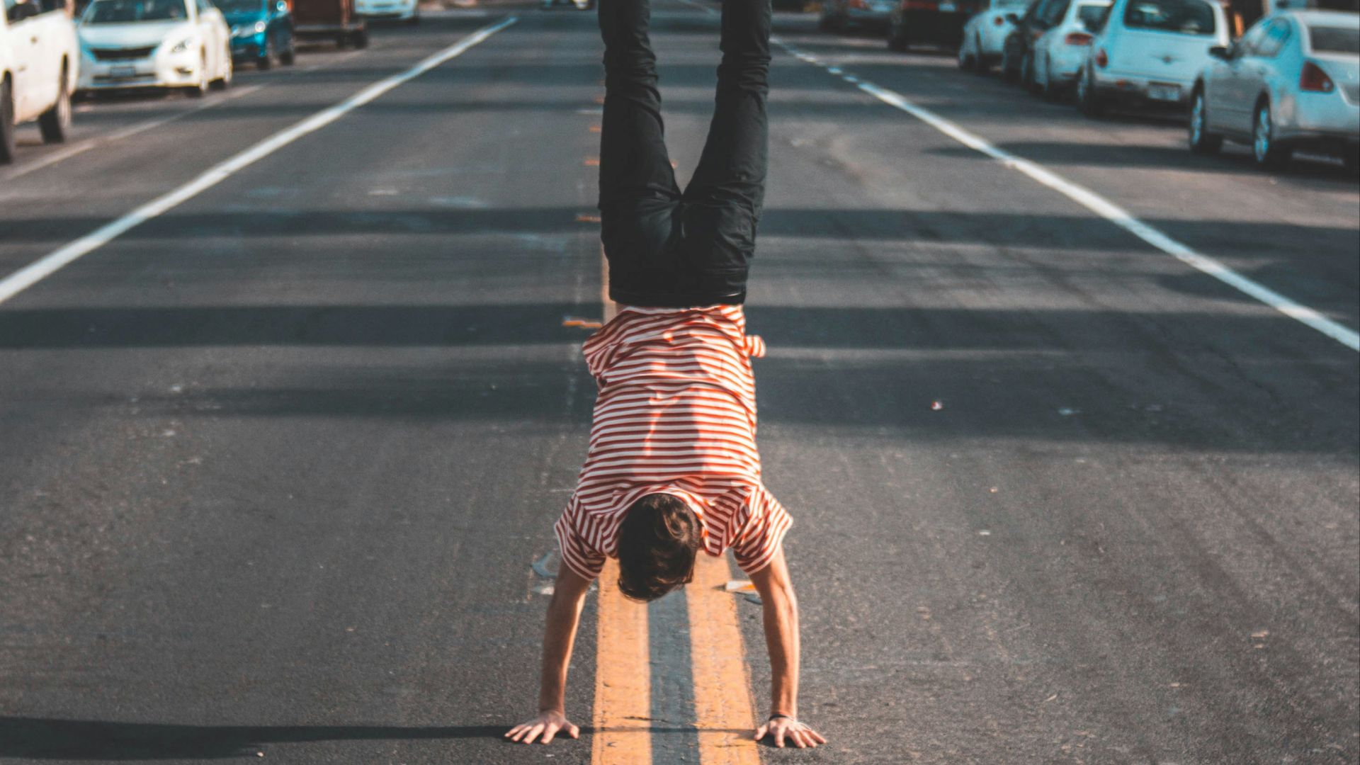 man doing hands stand on asphalt road between trees