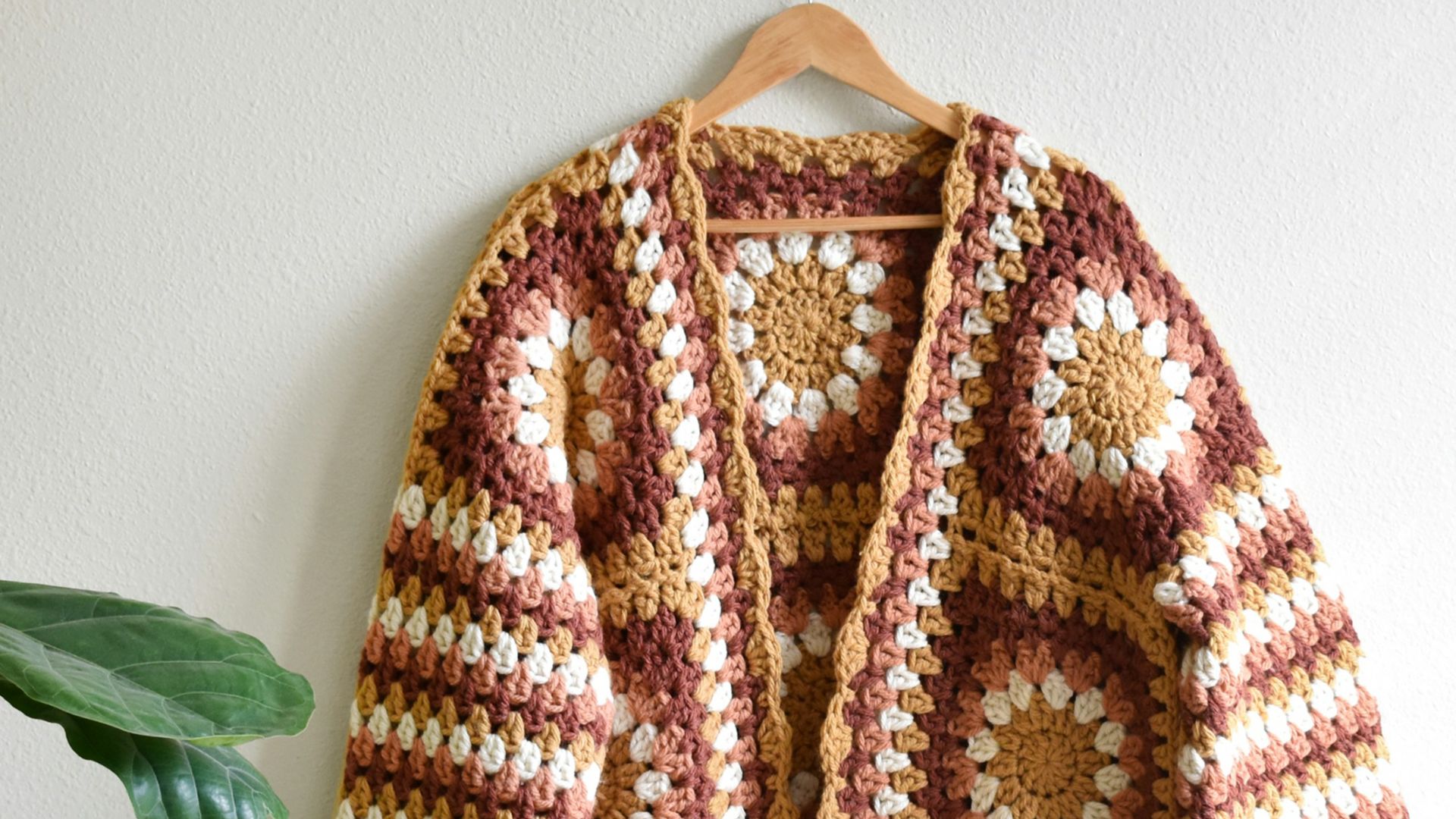 a crocheted jacket hanging on a wall next to a potted plant