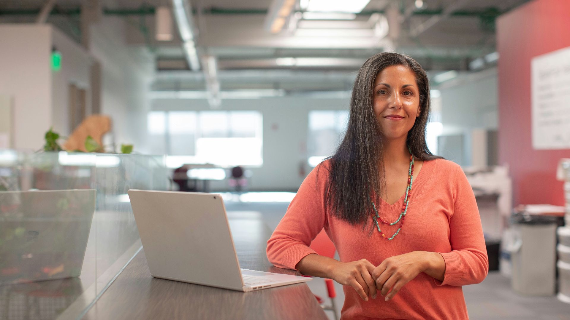 woman in orange long sleeve shirt sitting beside table with macbook pro