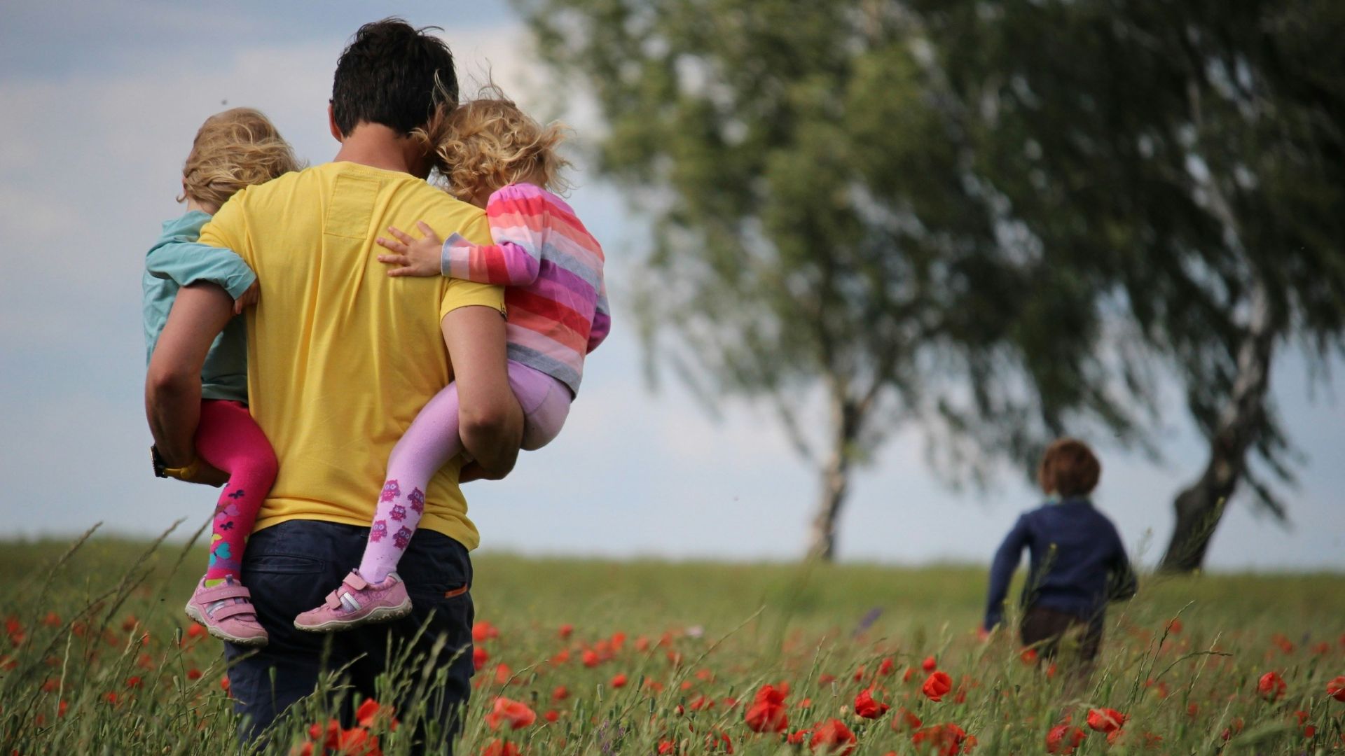 man carrying to girls on field of red petaled flower