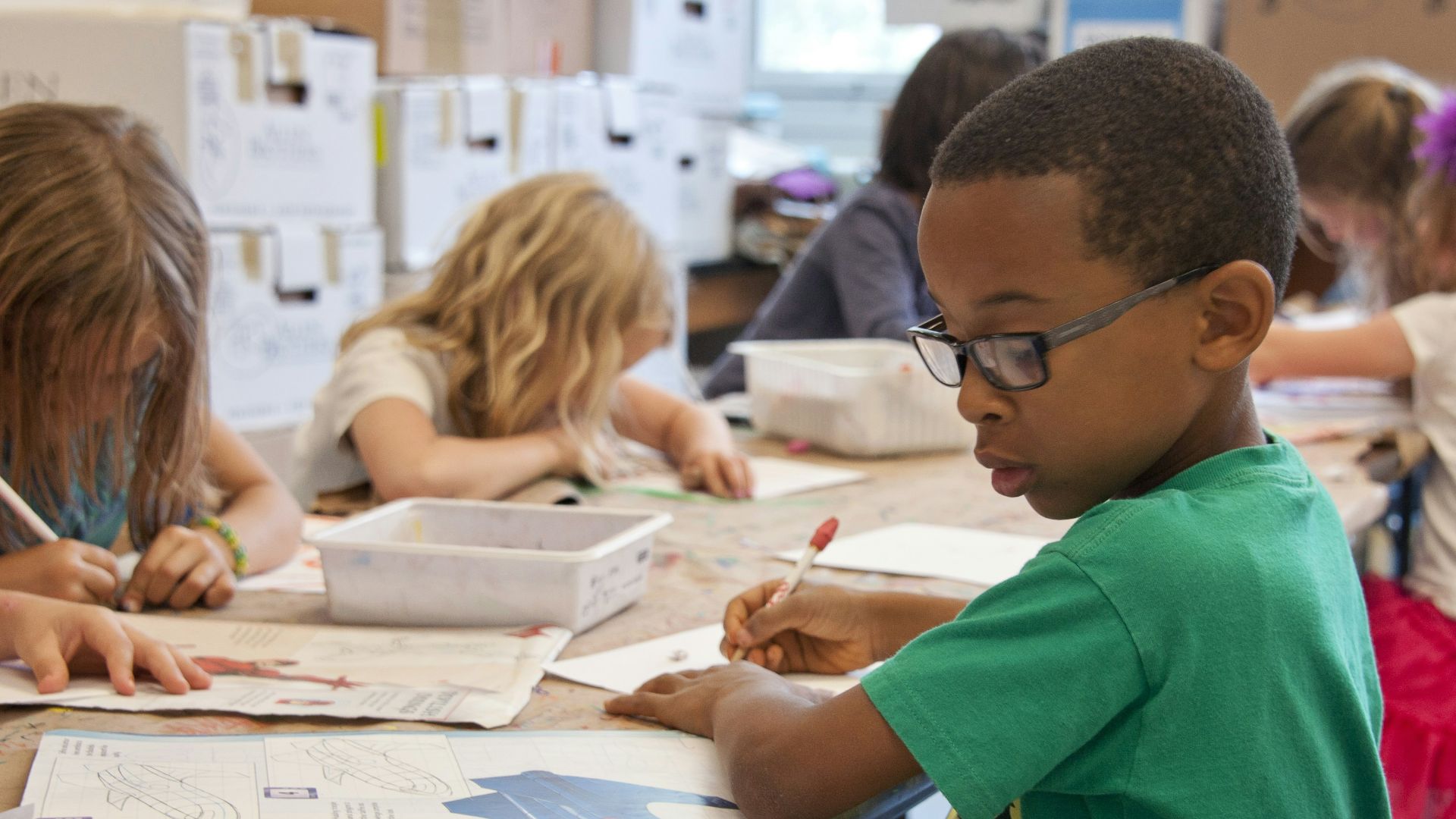 boy in green sweater writing on white paper