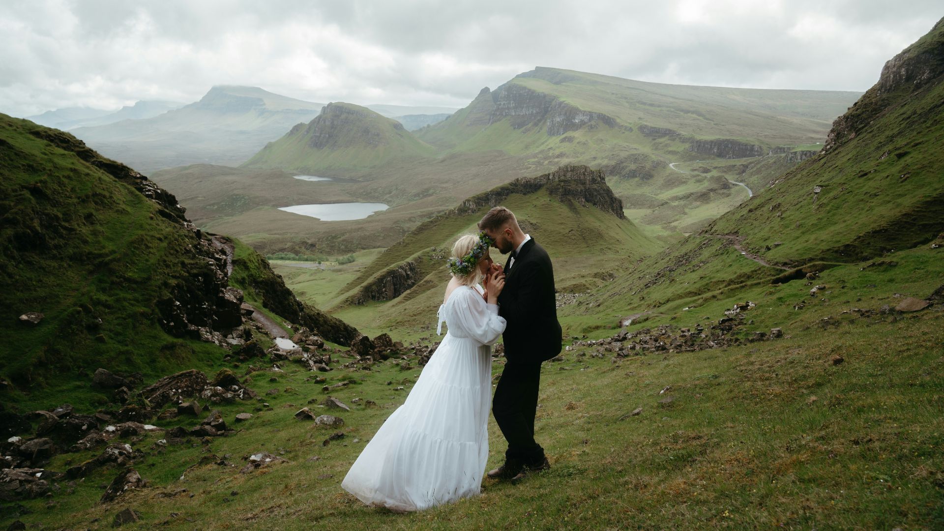 A bride and groom standing on a grassy hill