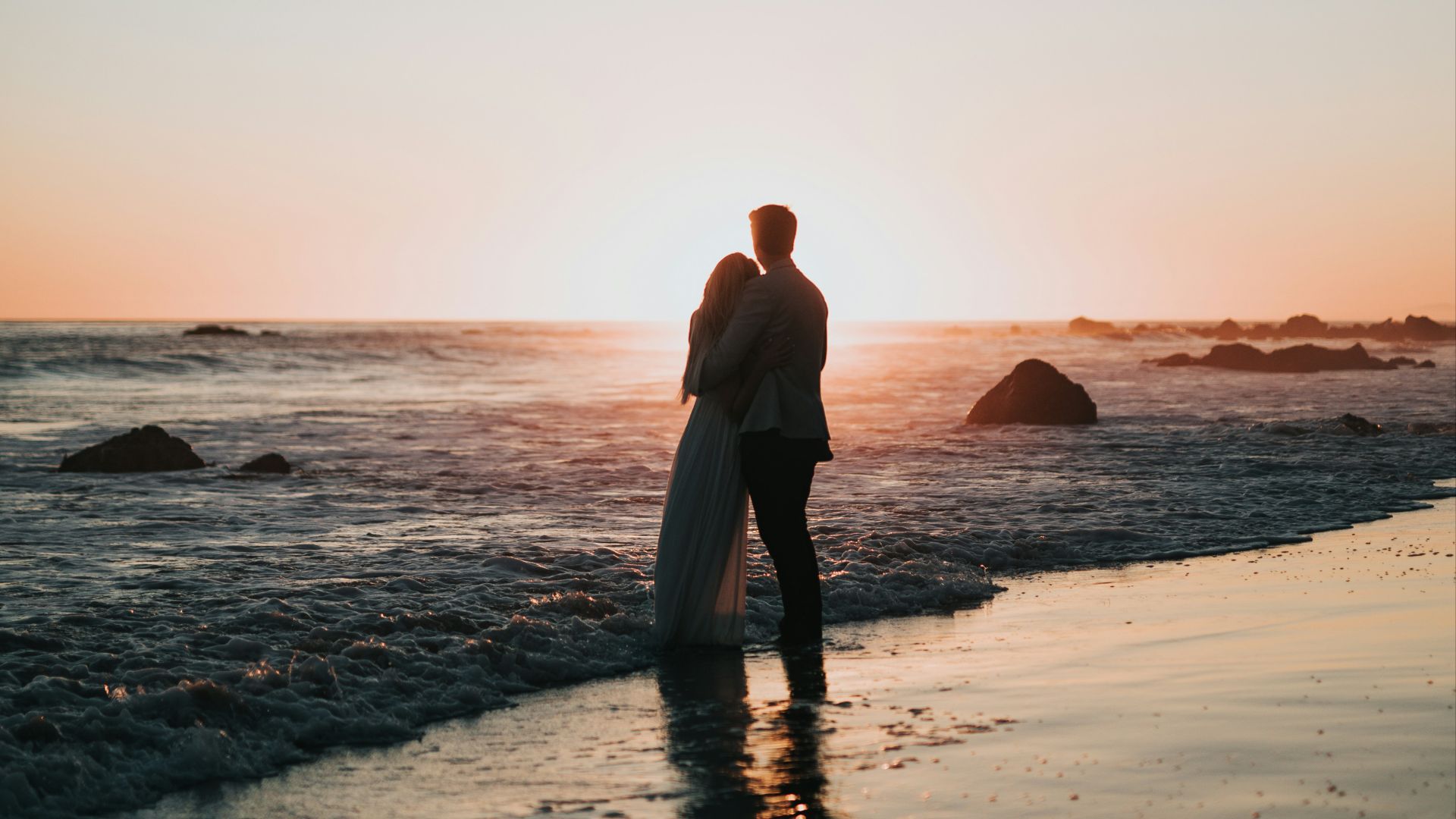 silhouette photo of couple standing on beach watching sunset
