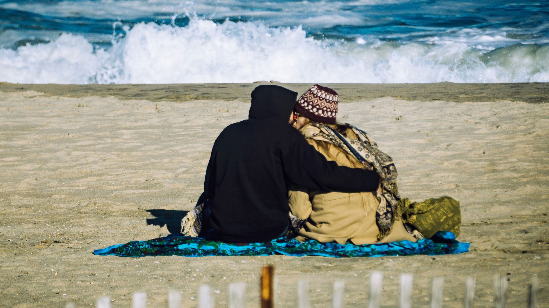person in black hoodie sitting on beach sand during daytime