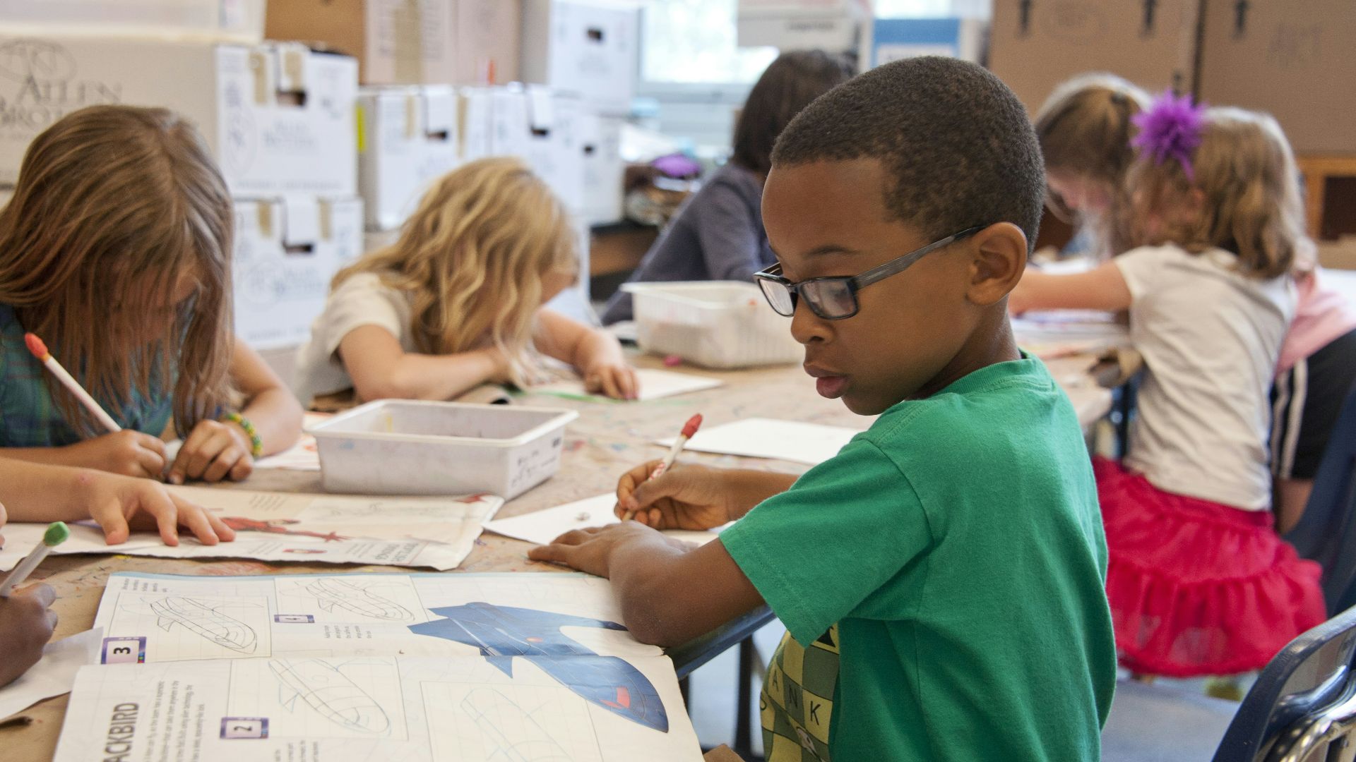 boy in green sweater writing on white paper