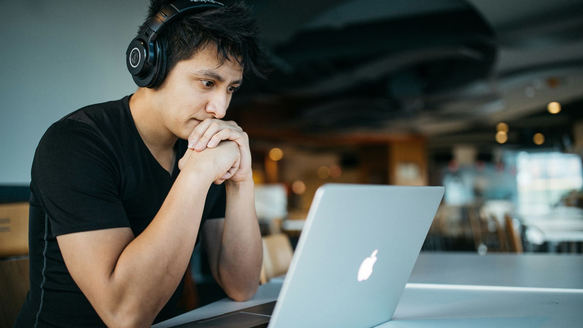man wearing headphones while sitting on chair in front of MacBook