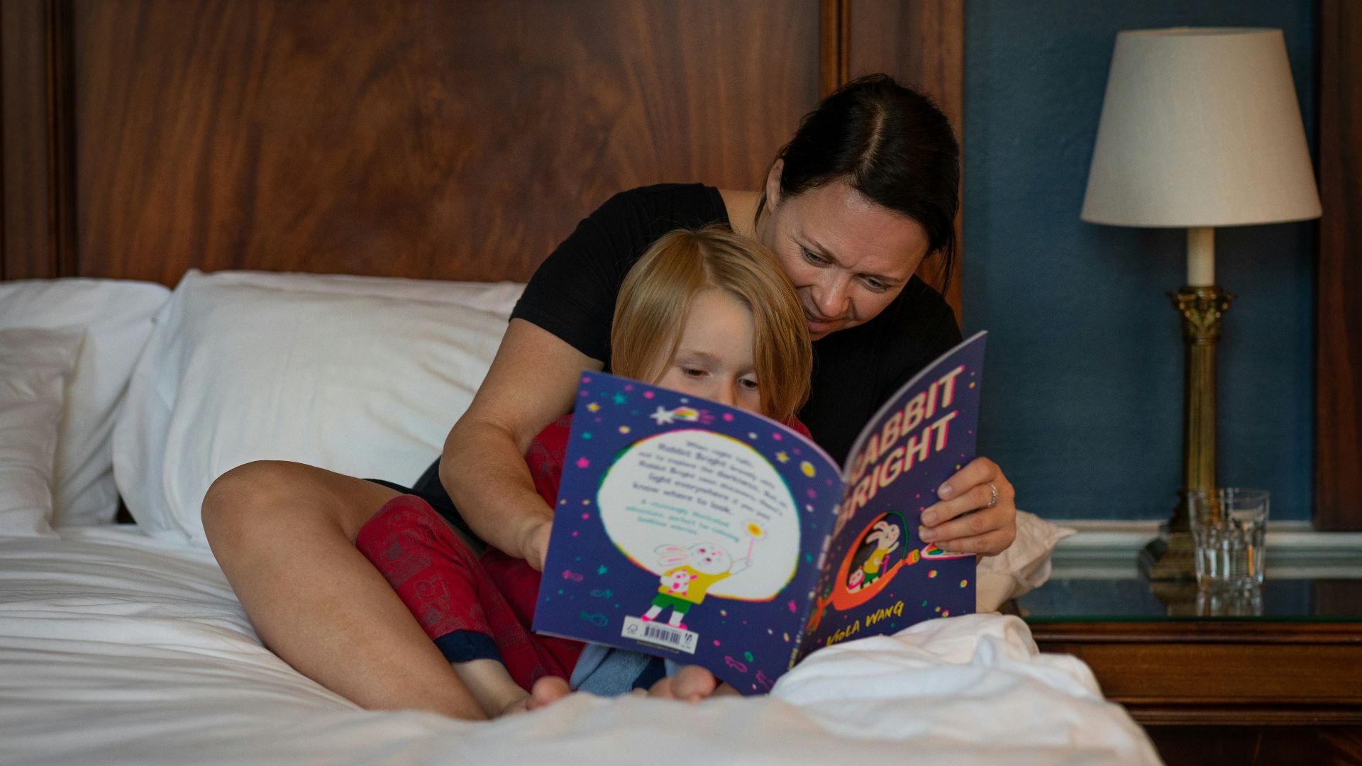 girl in red shirt lying on bed reading book