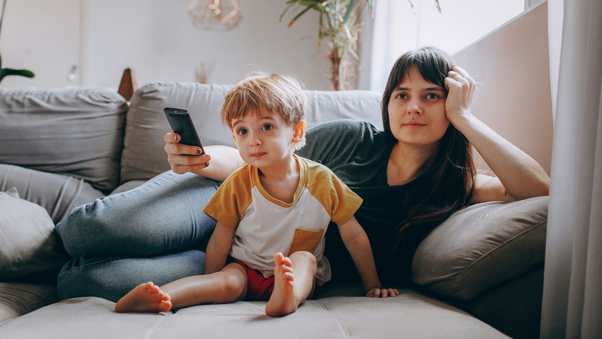 a woman and a child sitting on a couch looking at a cell phone