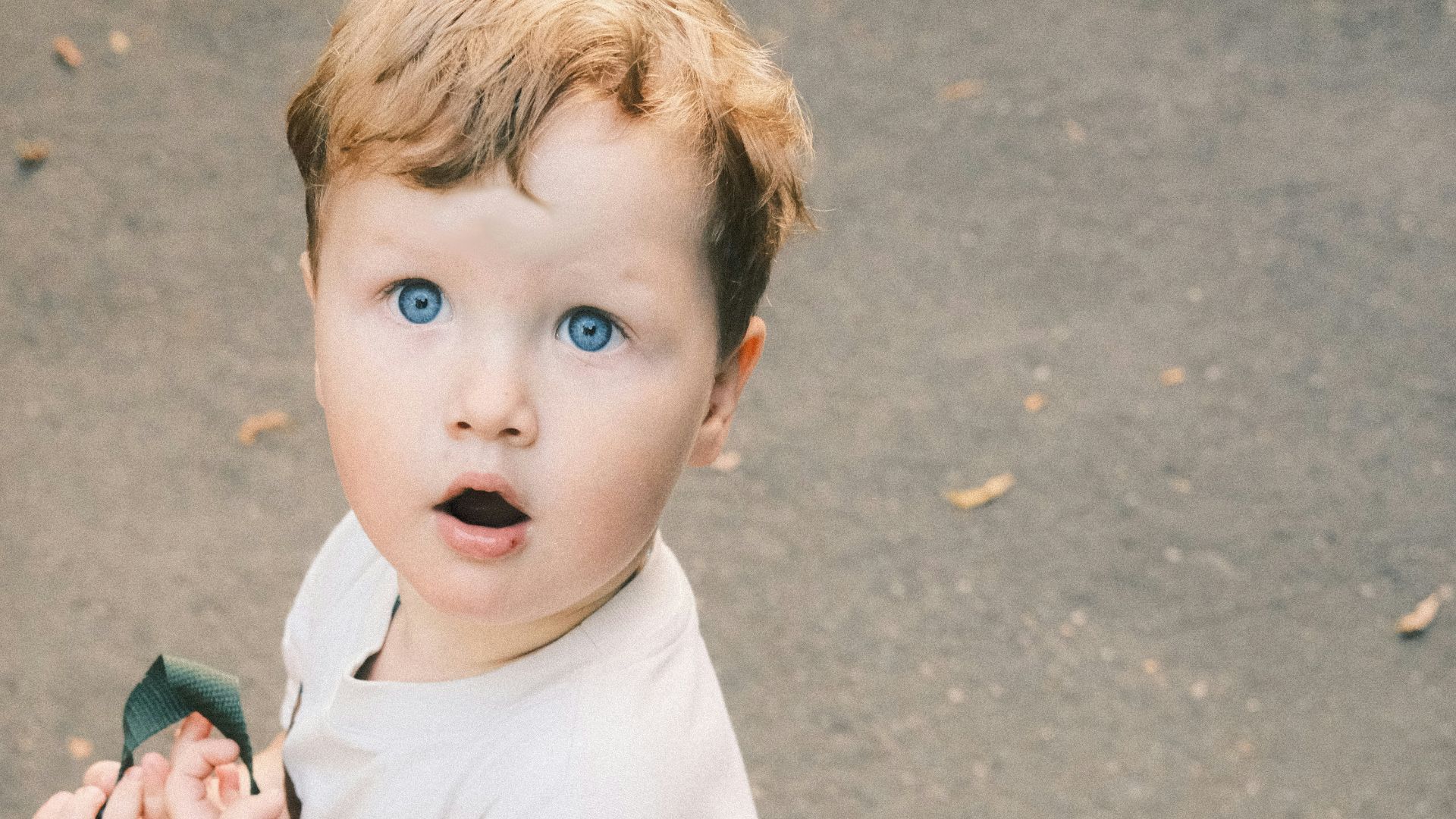 a little boy standing on a sidewalk holding a backpack