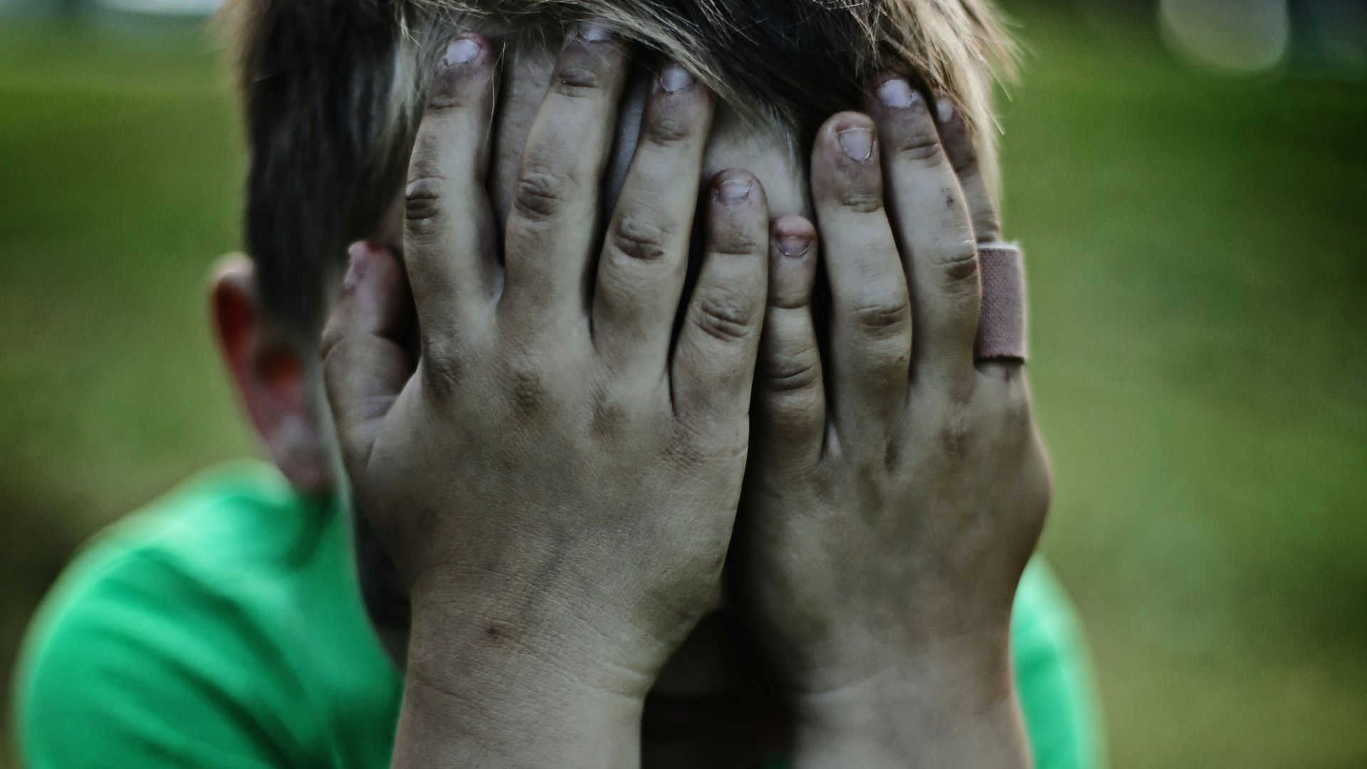 boy sitting while covering his face