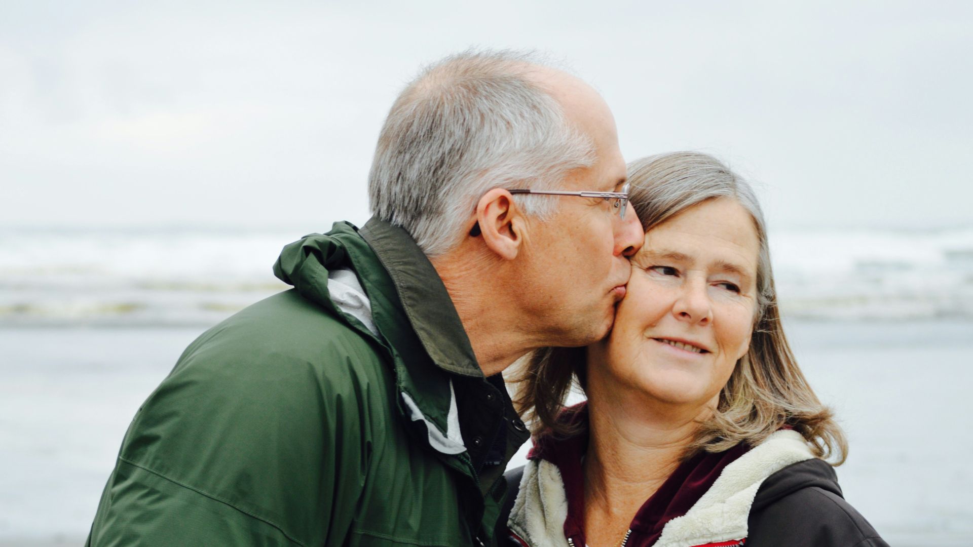 man kissing woman on check beside body of water