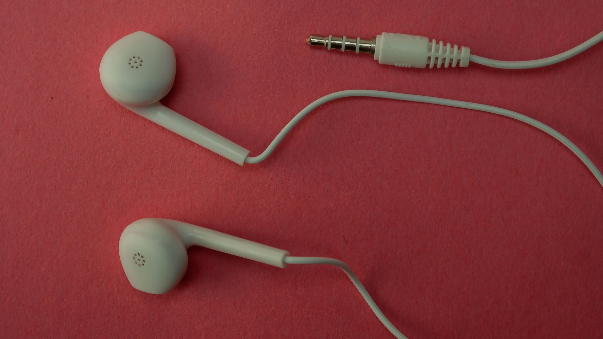White earbuds and their cable on a pink surface.