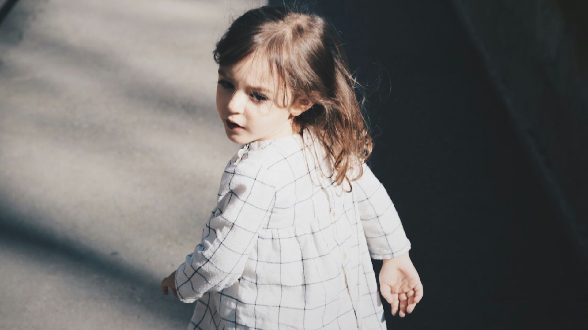 toddler girl walking on gray concrete road at daytime