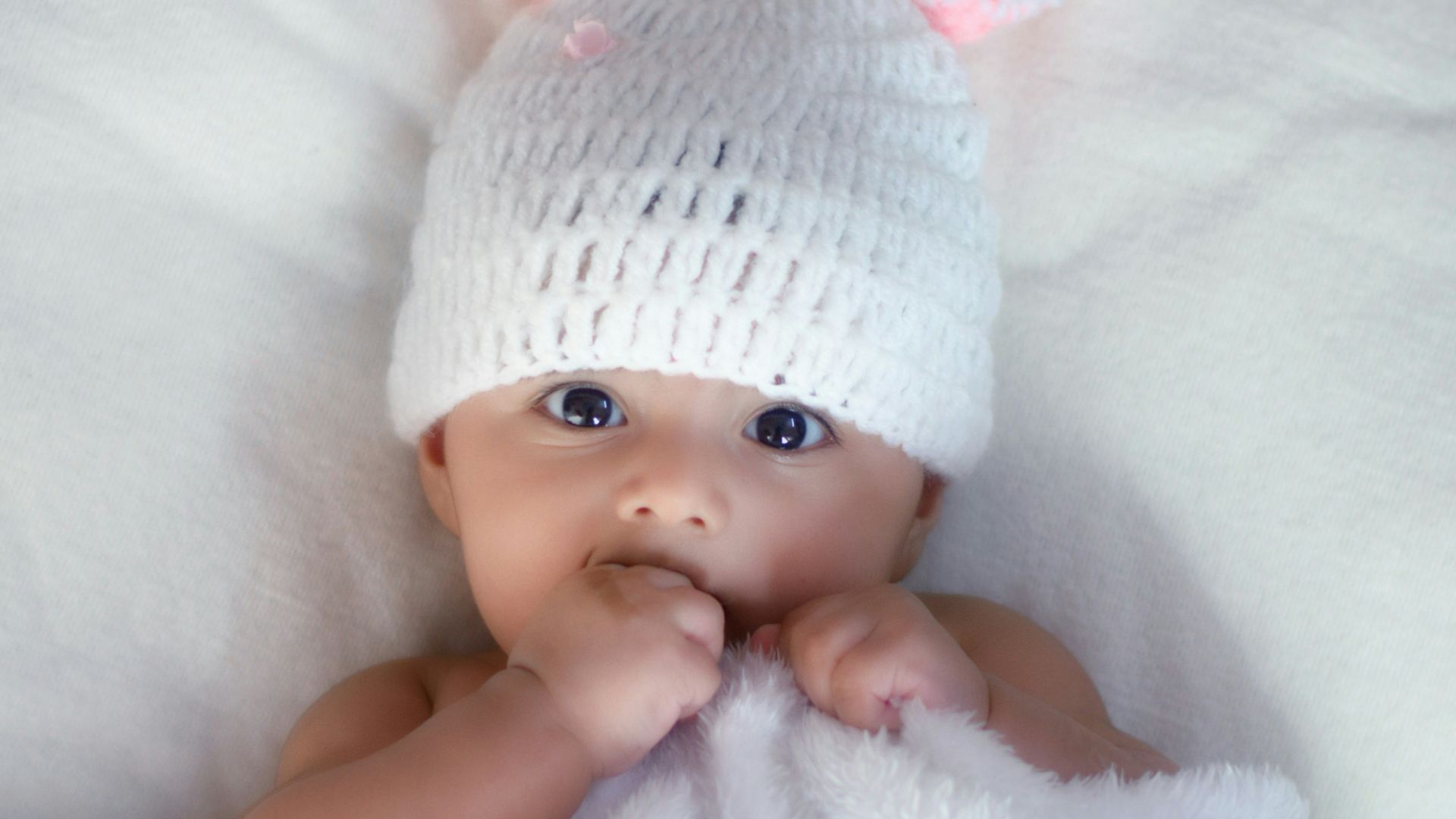 baby in white knit cap lying on white textile