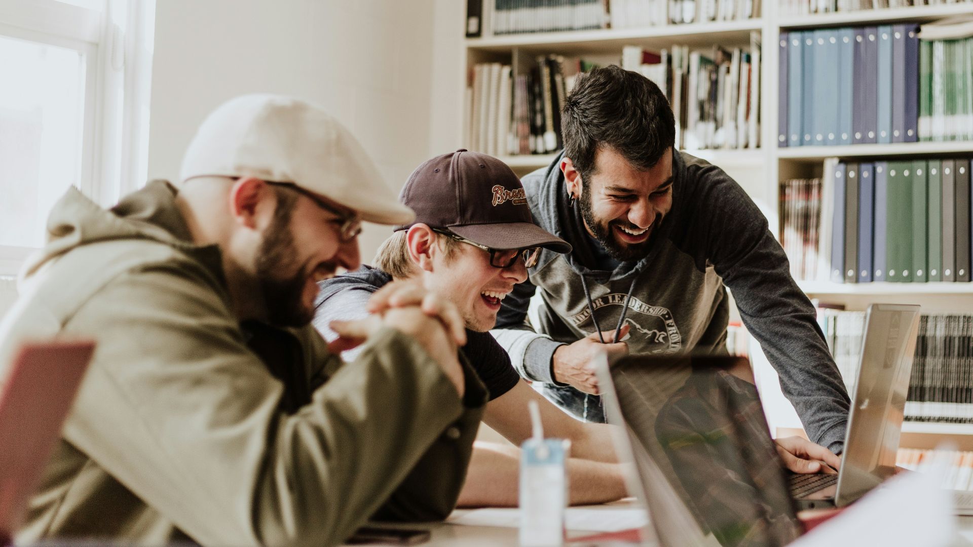 three men laughing while looking in the laptop inside room