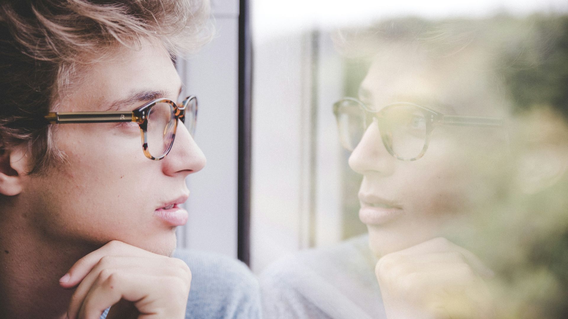 a man wearing glasses looking out a window