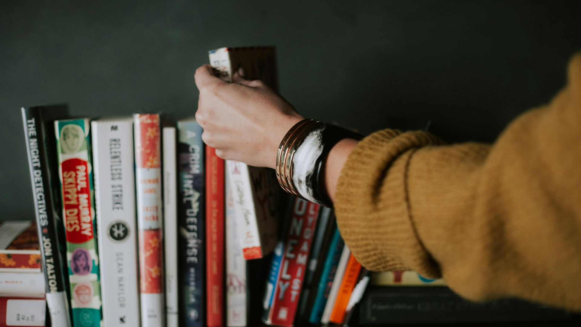 person picking white and red book on bookshelf