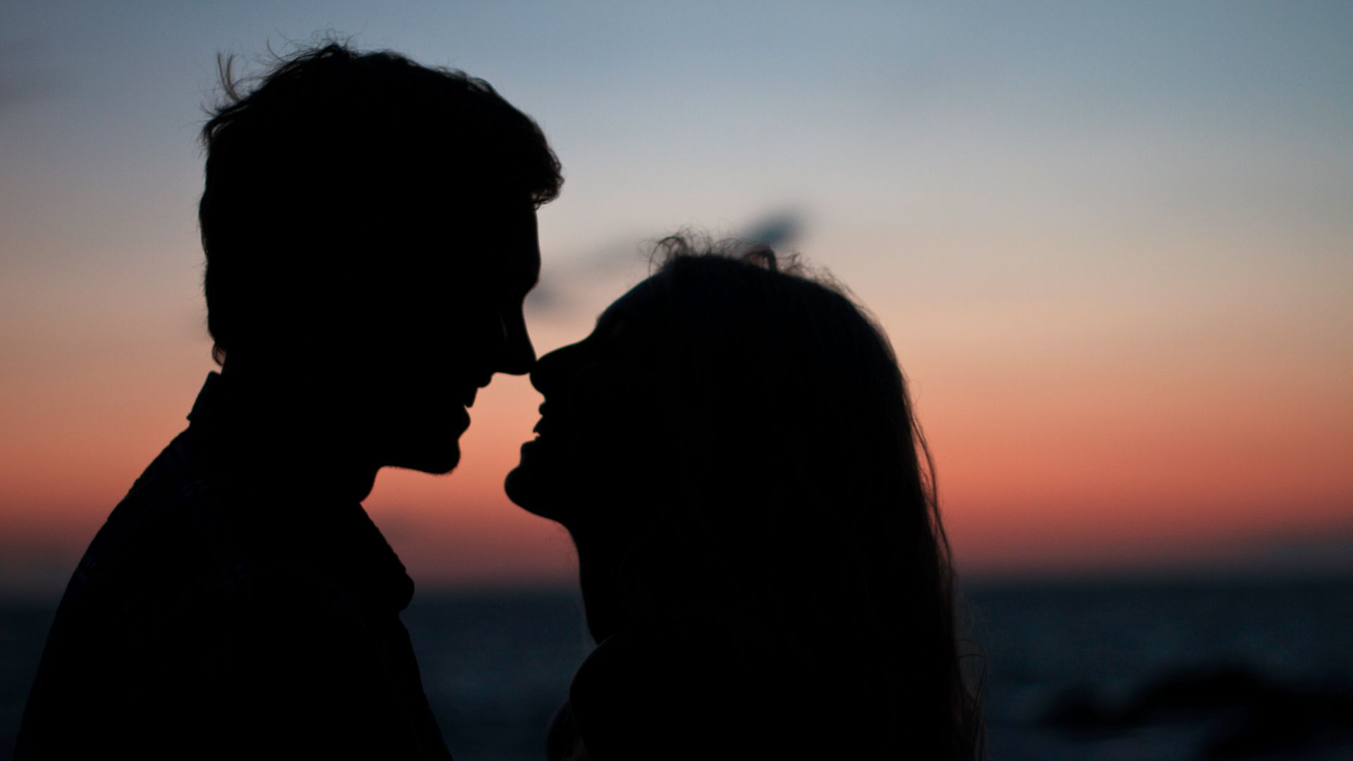 silhouette of man and woman about to kiss on beach during sunset