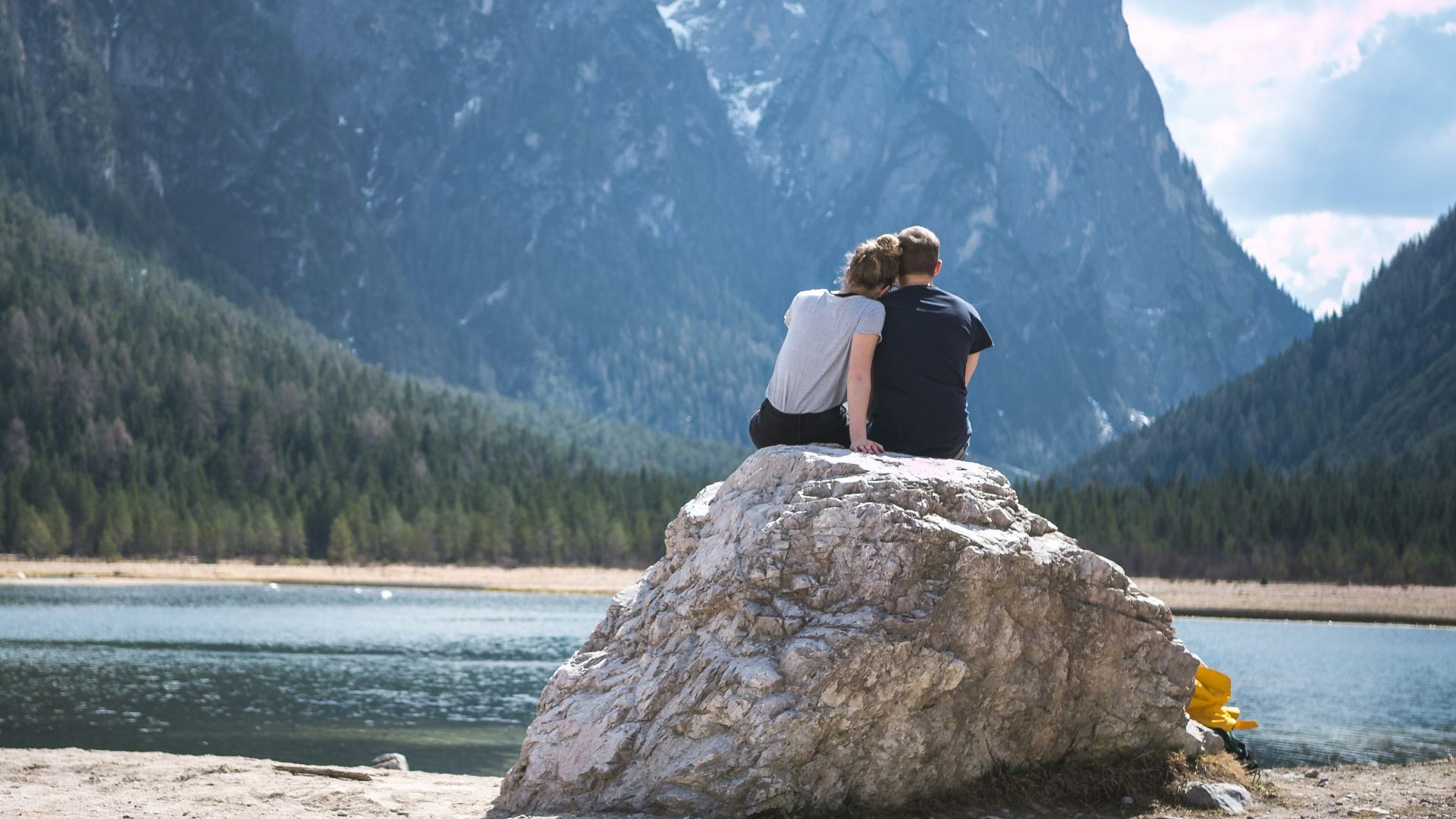 a couple sits on a rock looking out over a lake