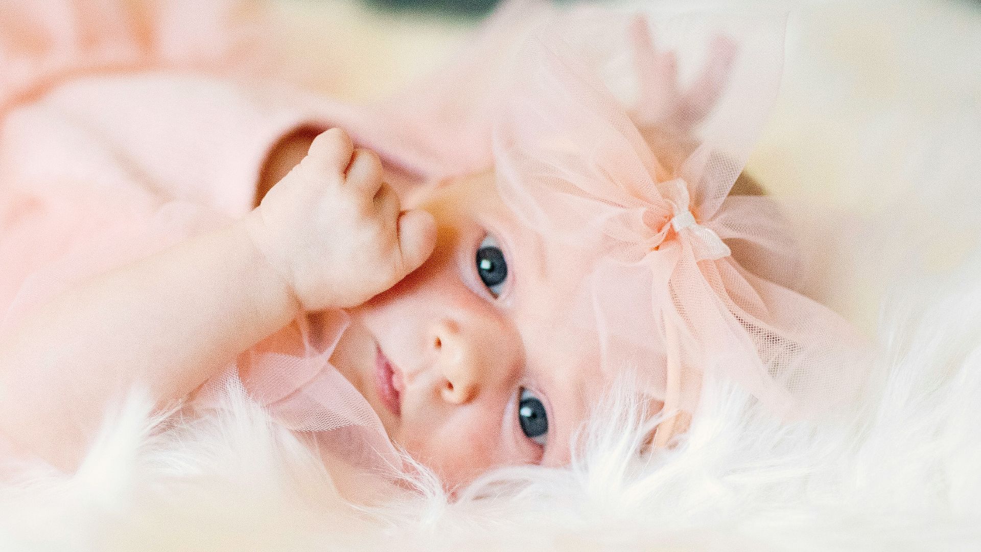 A baby in a pink dress laying on a fluffy white blanket