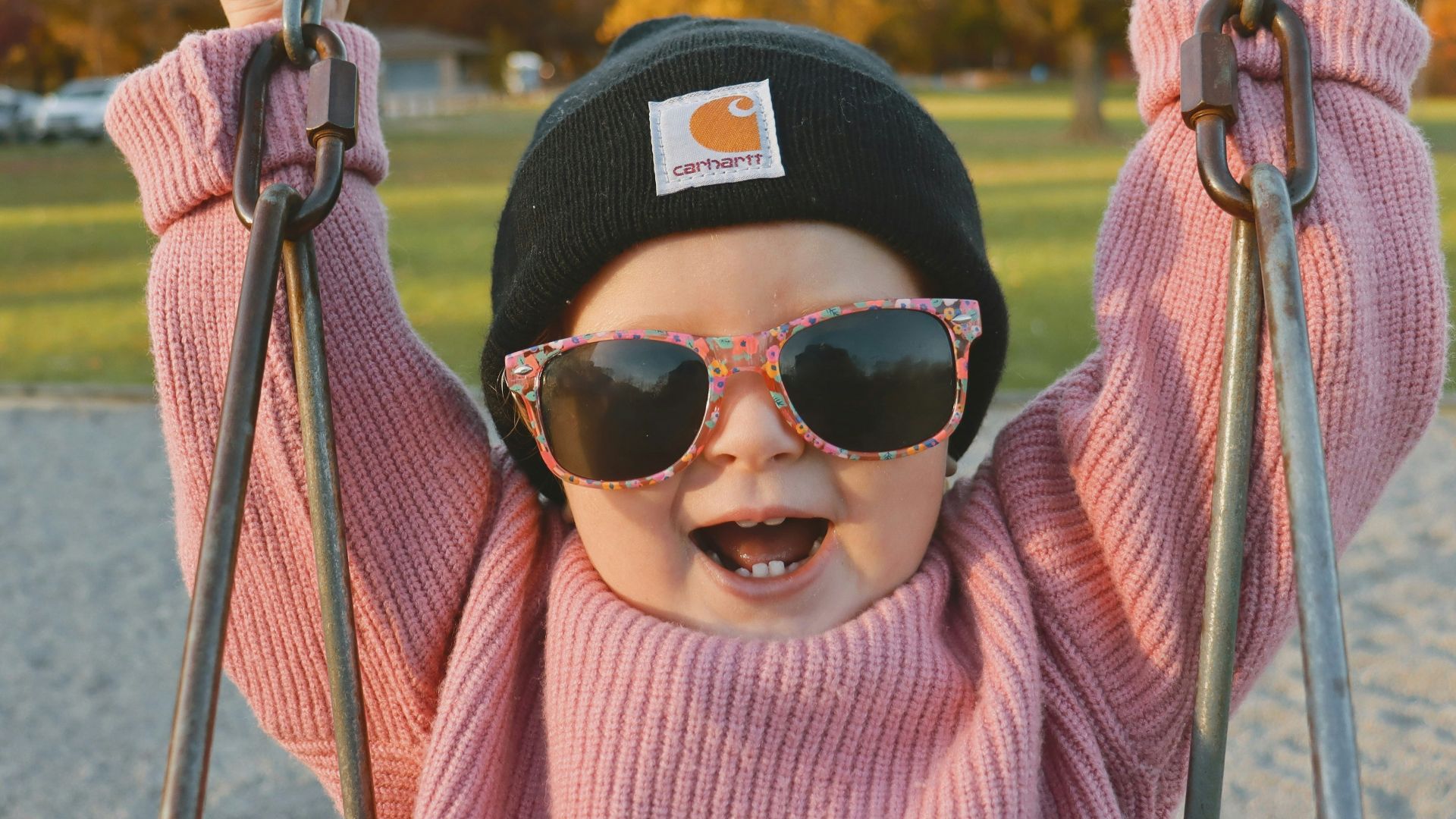 a little girl wearing sunglasses and a hat on a swing