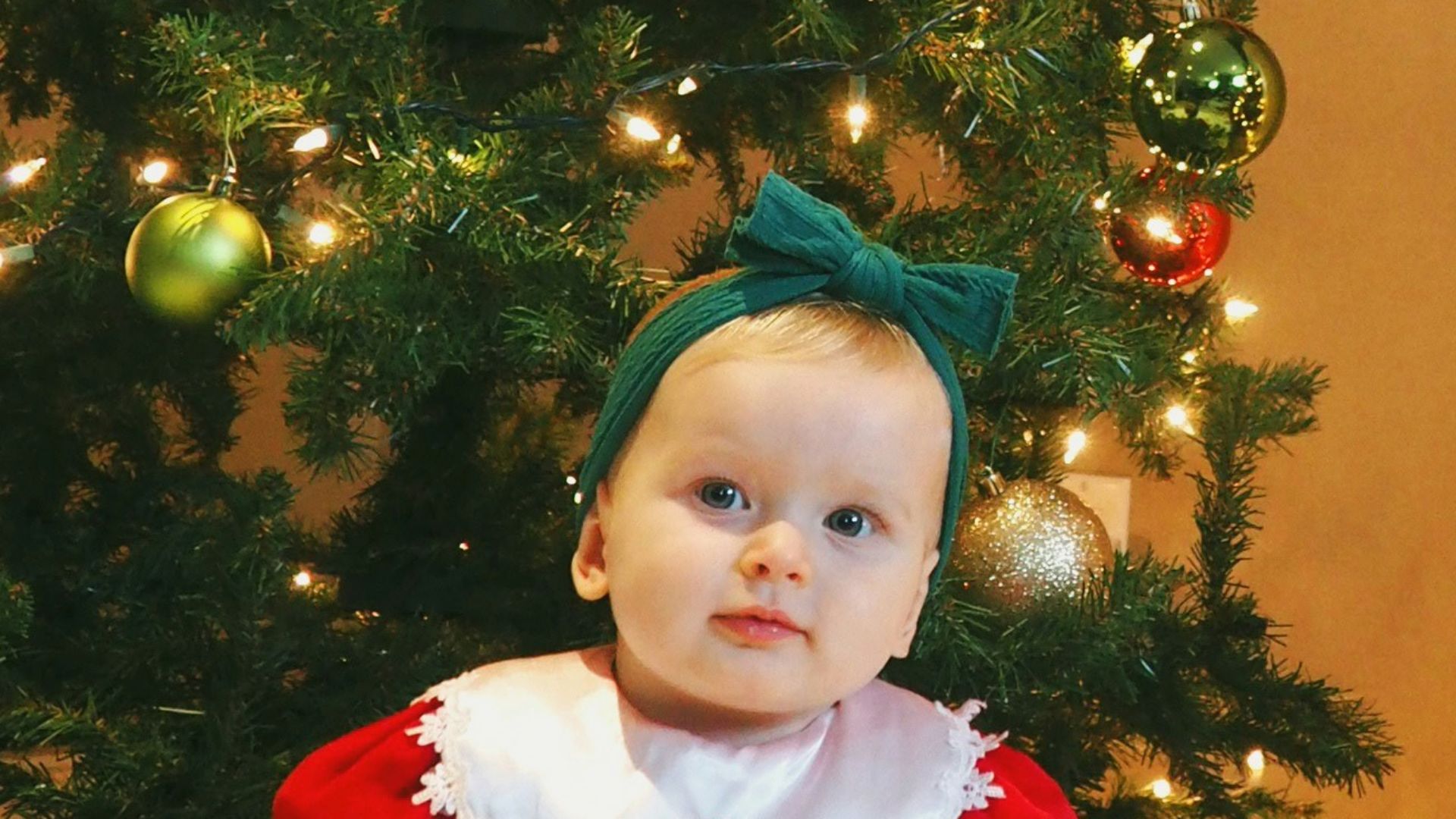 girl in red and white santa costume standing beside green christmas tree
