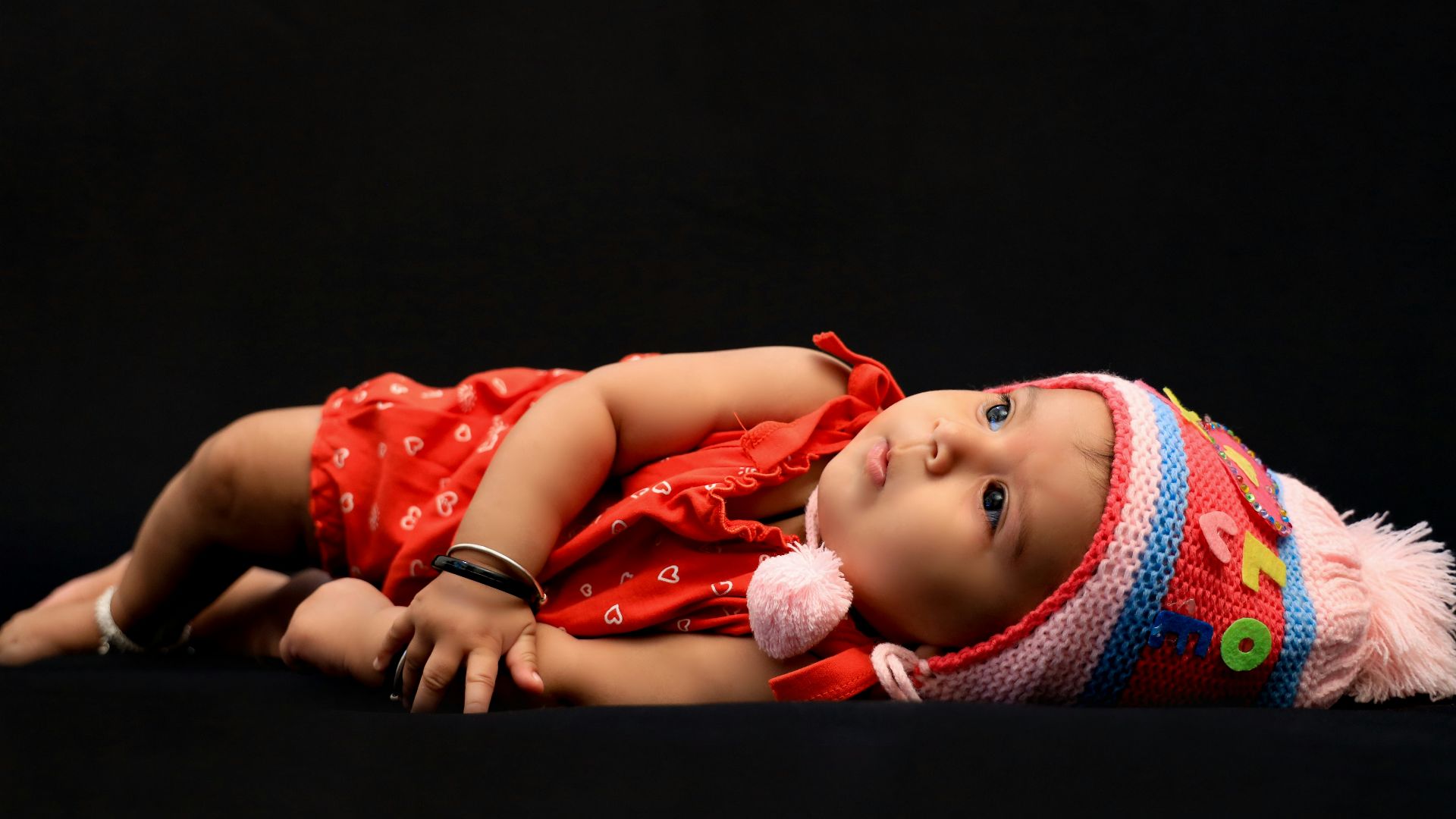 baby in red shirt lying on black textile