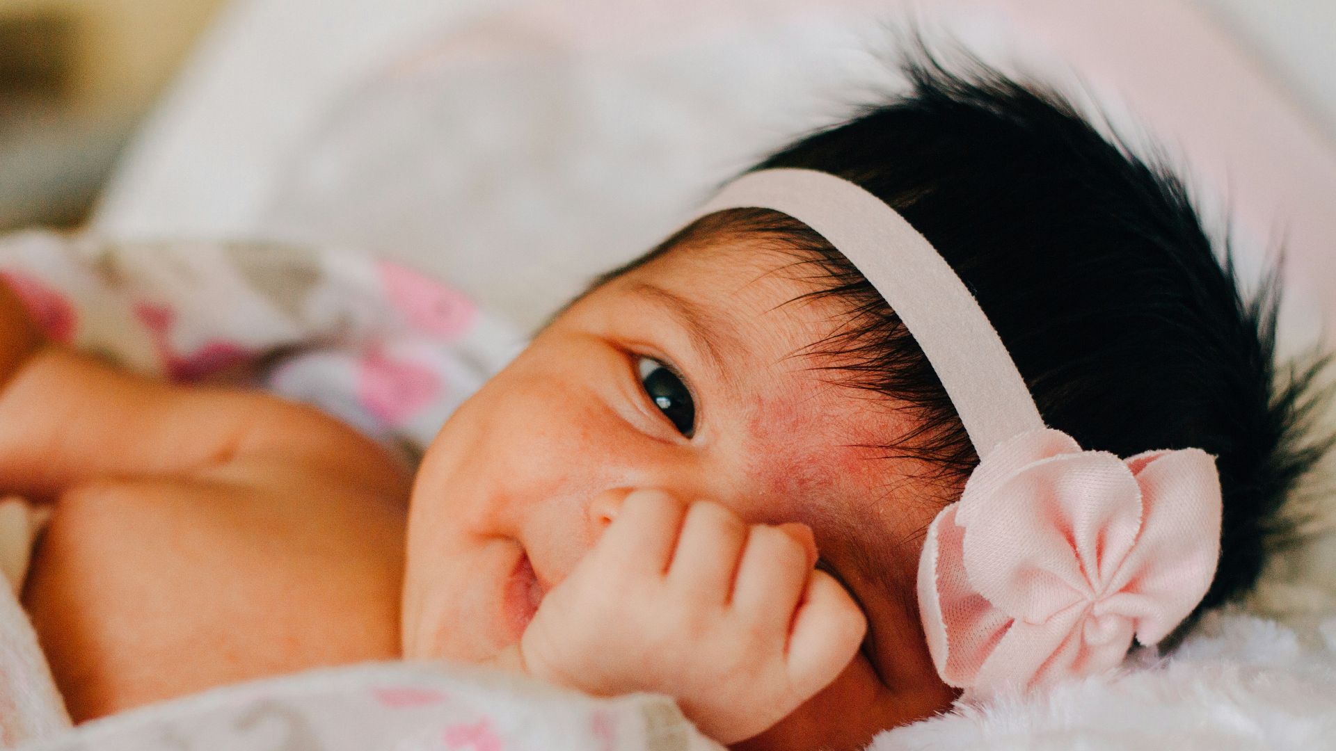 baby wearing white floral headband lying on bed while smiling