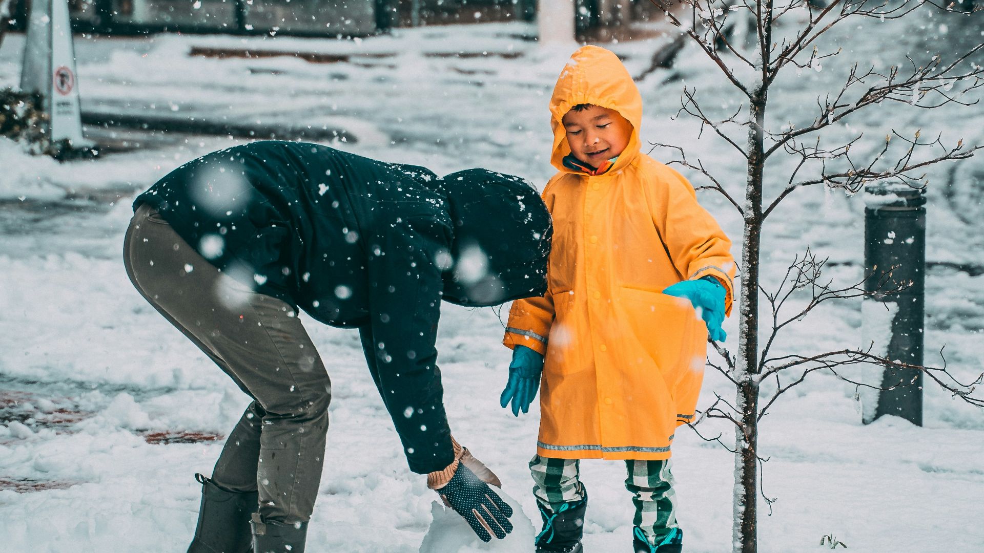 child in yellow jacket and black pants playing on snow covered ground during daytime