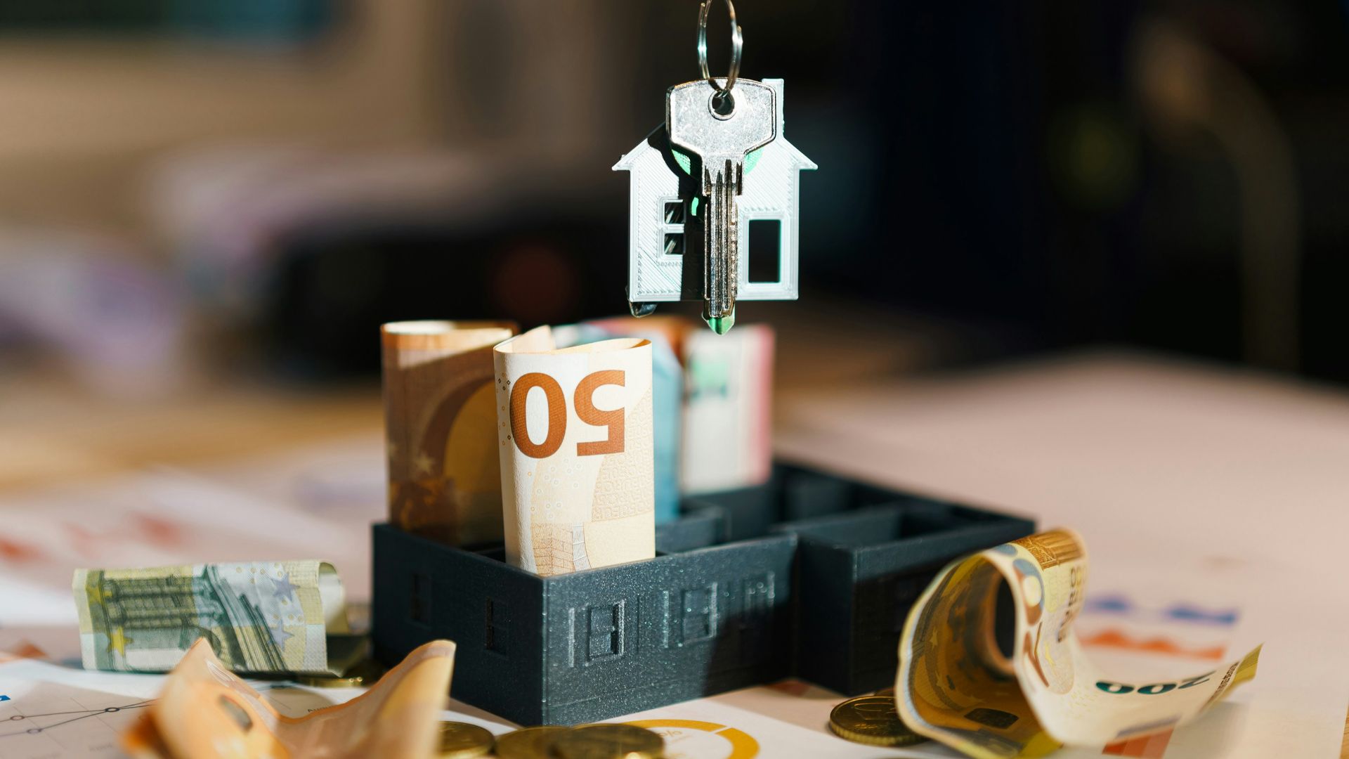 A house hanging from a string on top of a pile of money