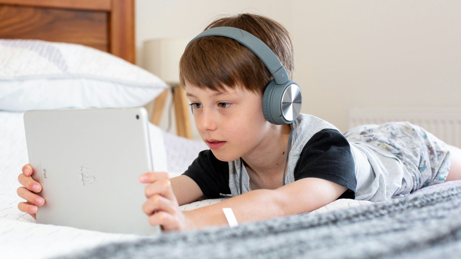 boy in blue shirt wearing headphones lying on bed