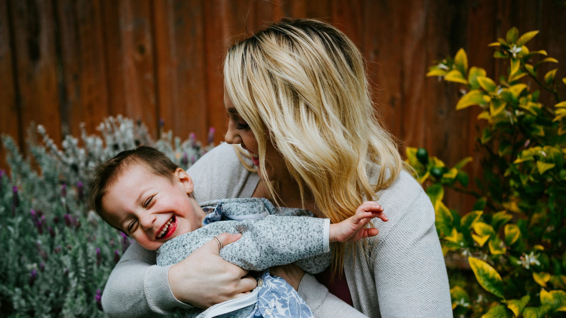 woman in gray sweater carrying girl in blue denim jacket