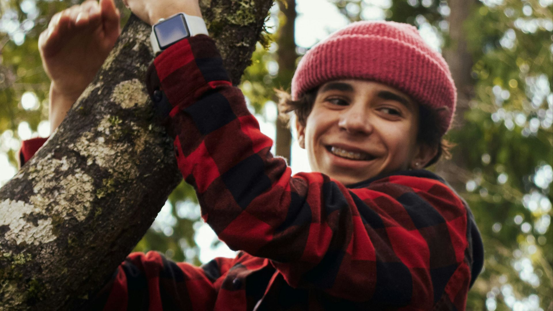 man in red and black plaid dress shirt and black pants sitting on tree branch during