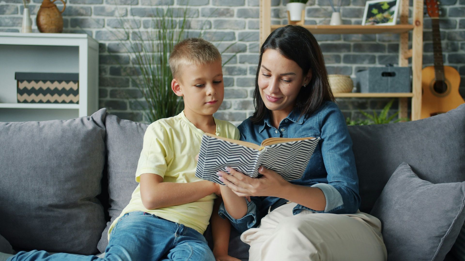 Mother and son reading a book together on sofa.