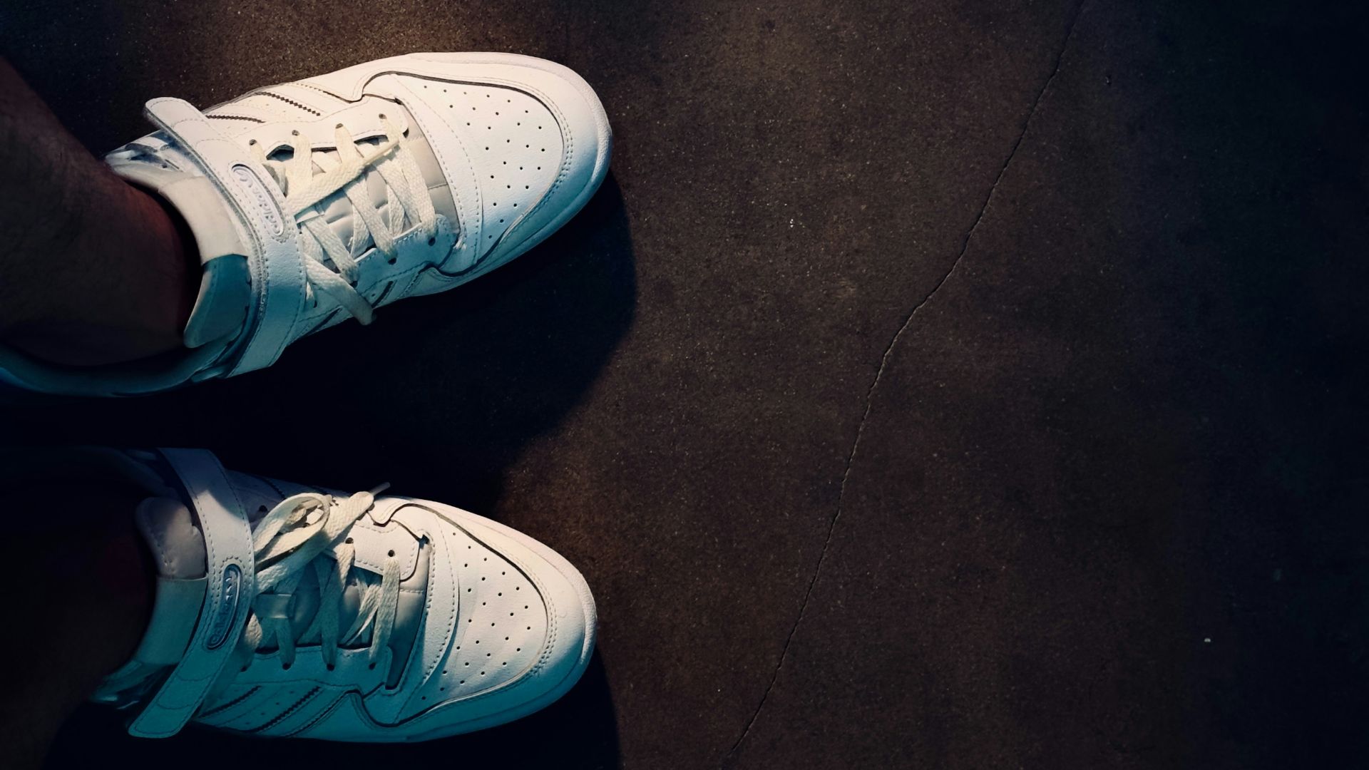 A person wearing white tennis shoes standing on a black floor