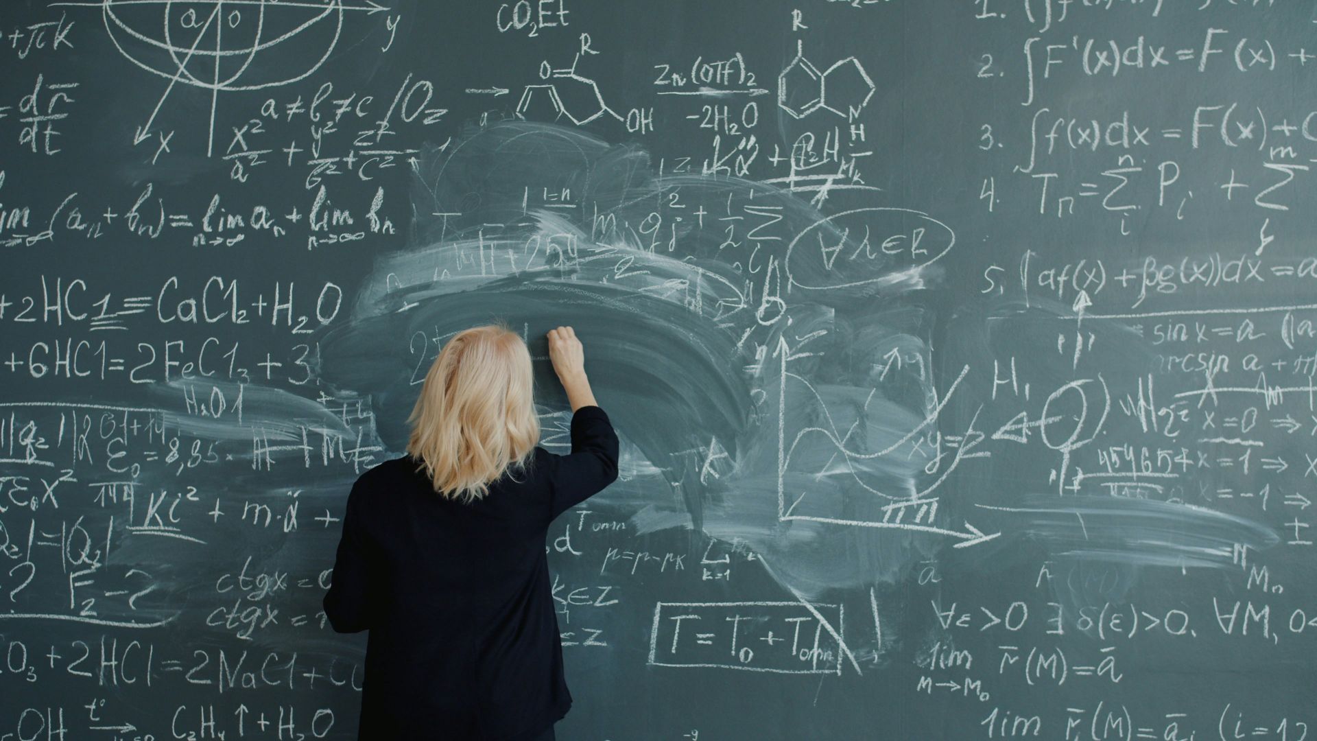 Woman writing complex mathematical formulas on a chalkboard.